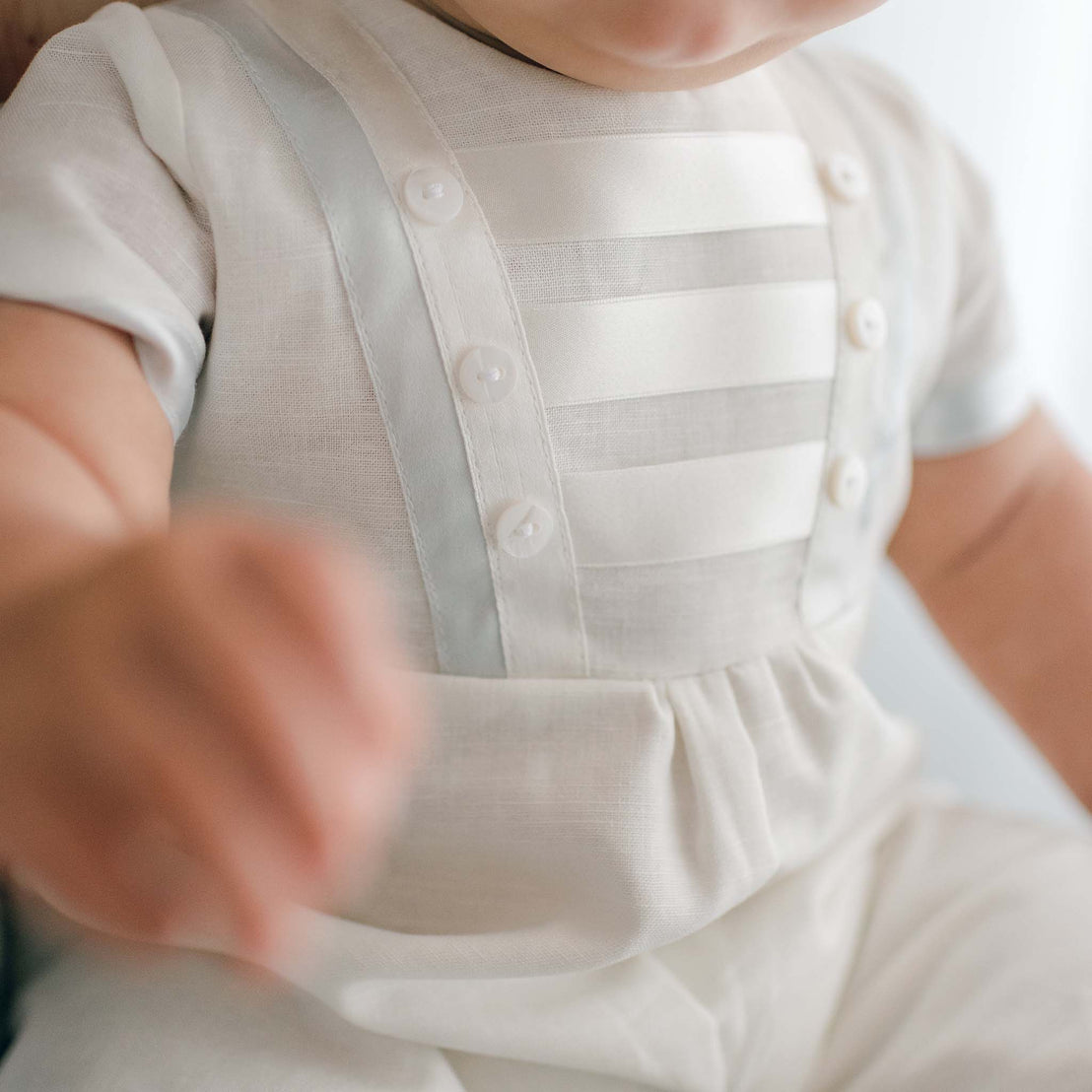 Close up photo showing the detail of the Owen Linen Romper with silk ribbon in ivory and light blue across the front