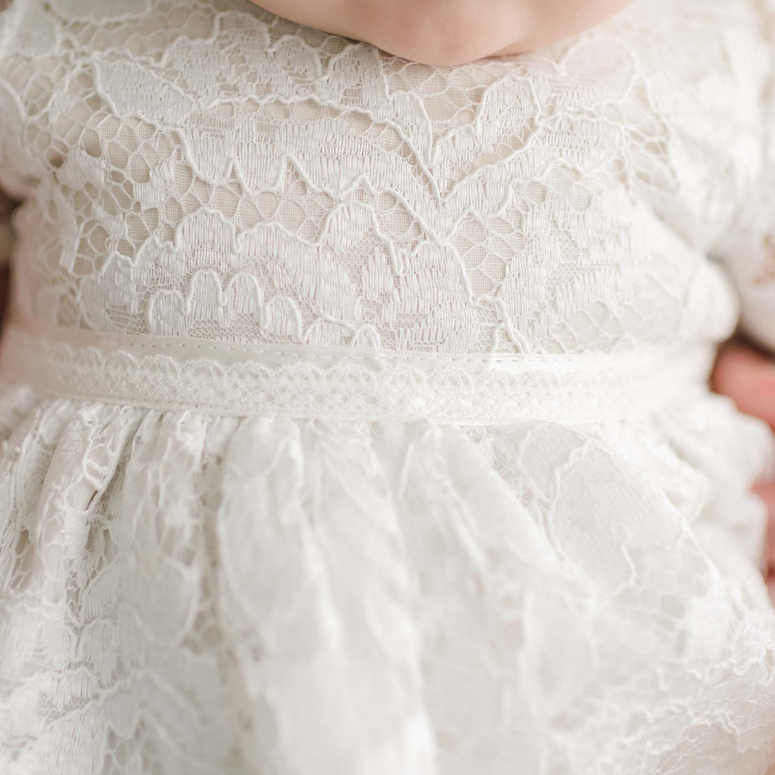 Close-up of a baby in the Rose Romper Dress, focusing on the detail of the lace and the stitching around the waistline. The texture of the lace is prominently featured.