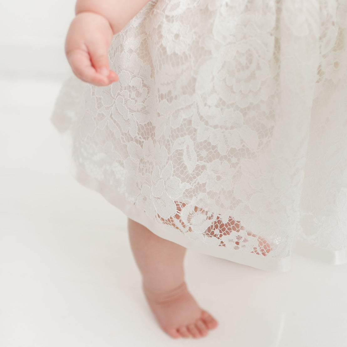 Close-up of a baby's lower legs and feet, one visible in focus. The baby is wearing the Rose Romper Dress. The background is white.