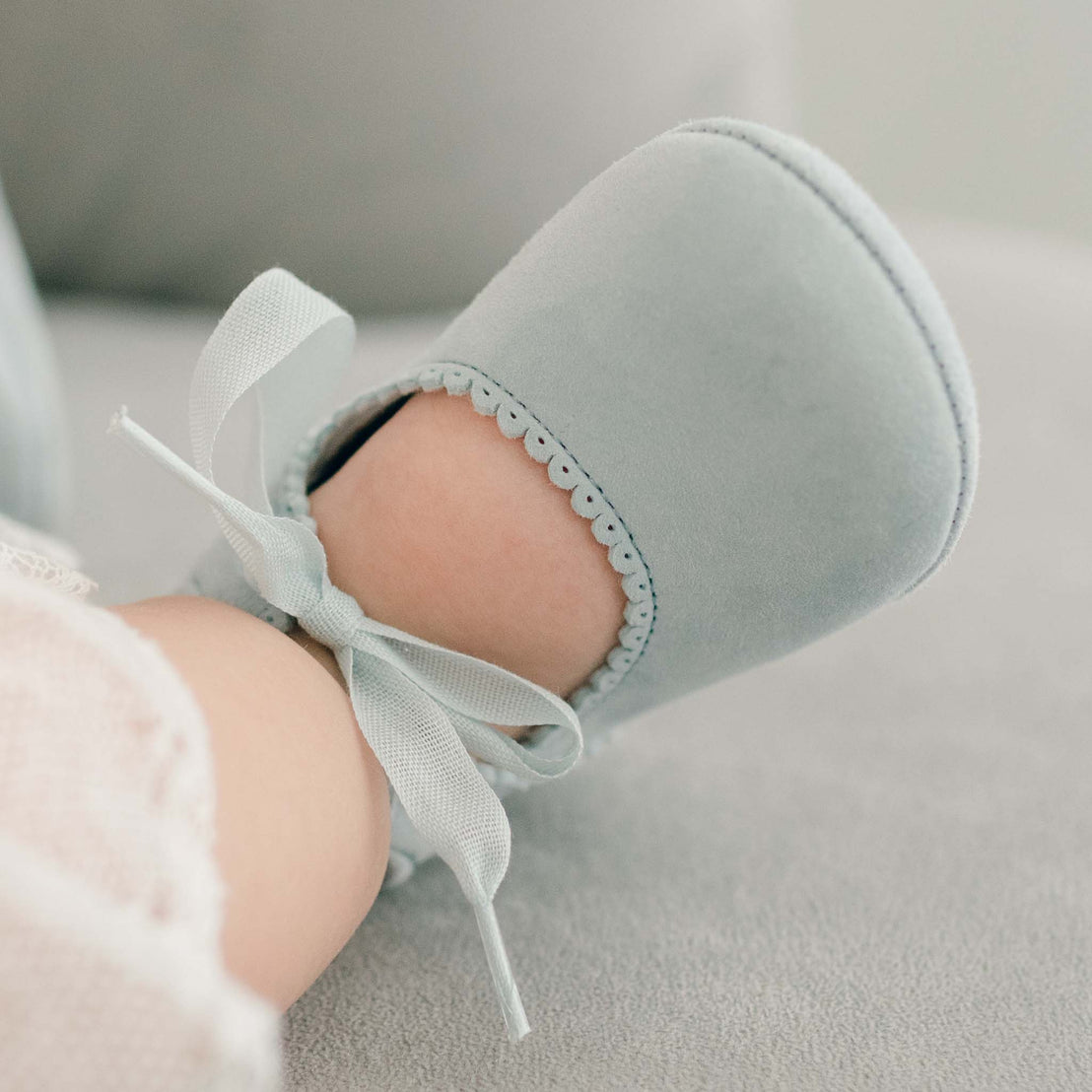 Baby girl wearing the sky blue Emily Suede Tie Mary Janes. Shoes are made with a soft suede with tie detail closure.