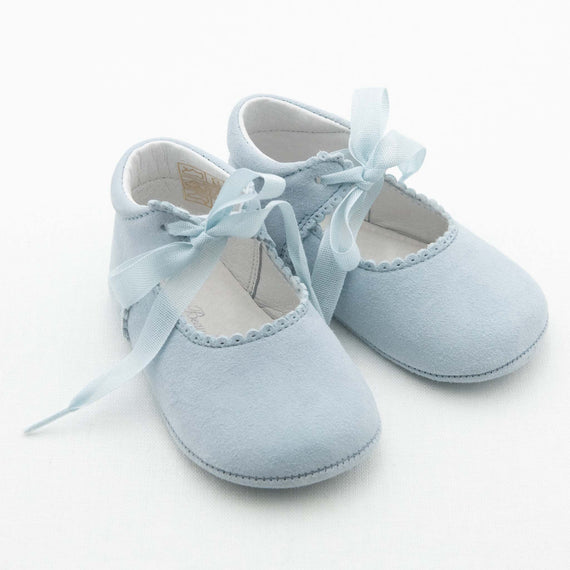 A pair of Sky Blue Suede Tie Mary Janes, handmade by Baby Beau & Belle from soft suede leather, features ribbon ties and scalloped edges. These baby shoes are positioned side by side on a pristine white background.