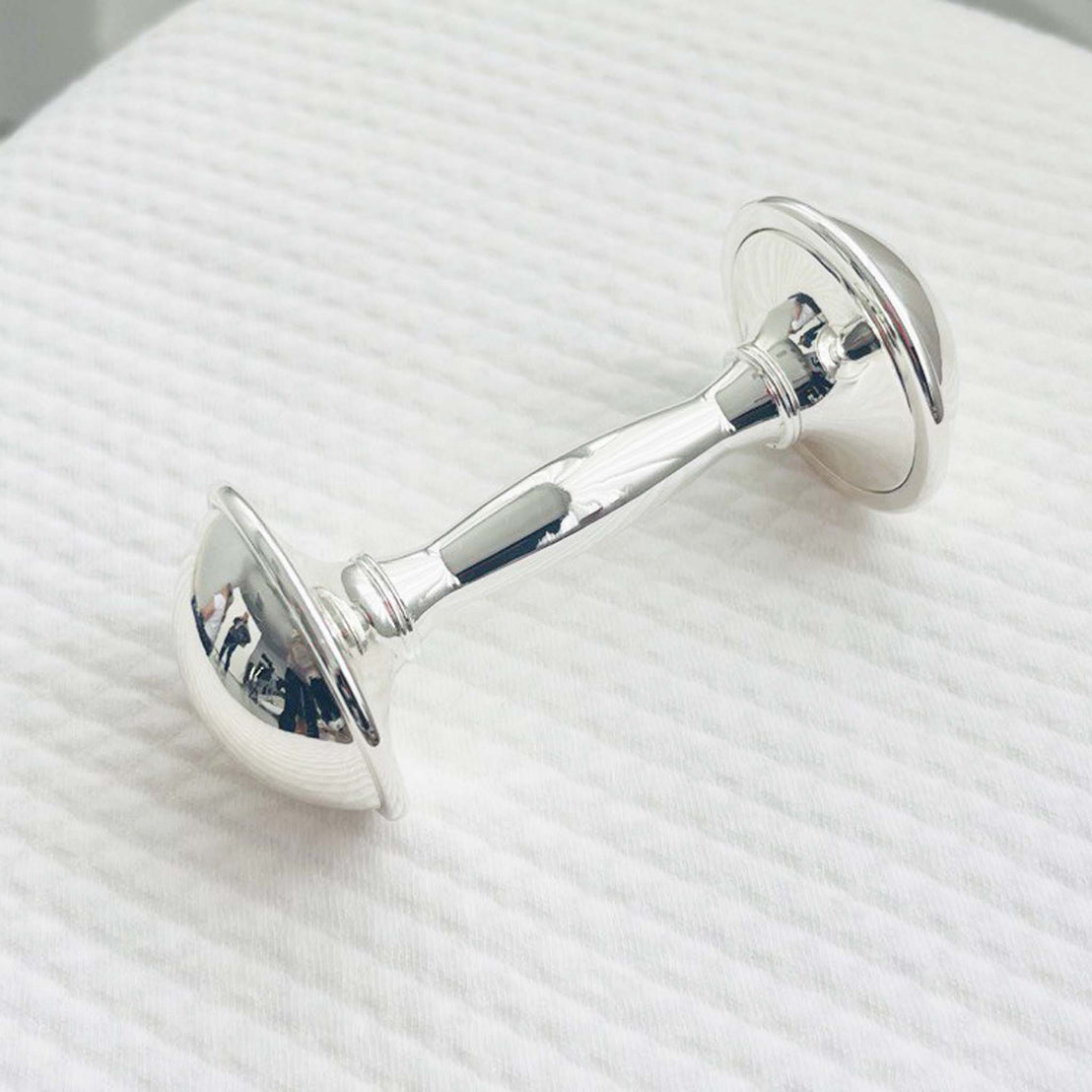 Silver plated dumbbell baby rattle on a white textured surface