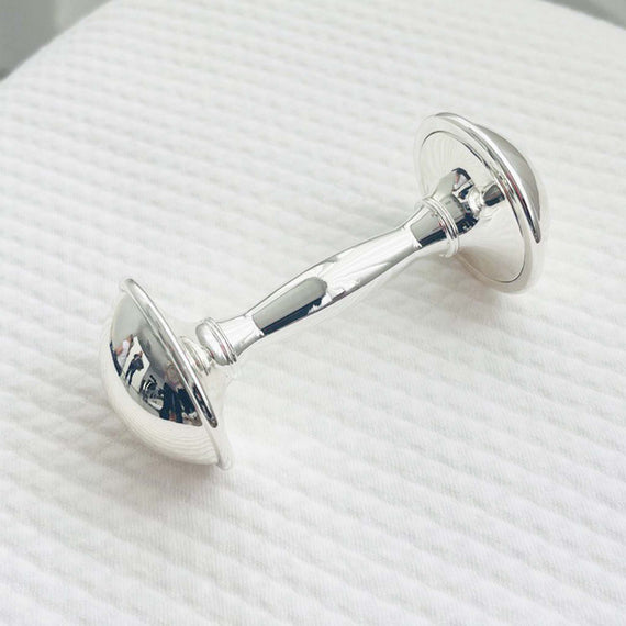 Silver plated dumbbell baby rattle on a white textured surface