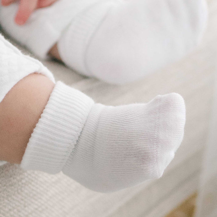 Close-up of a baby's foot wearing Girls Simple Socks, crafted from cotton nylon spandex, resting on a light-colored surface. The foot and sock are sharply in focus against a softly blurred background.