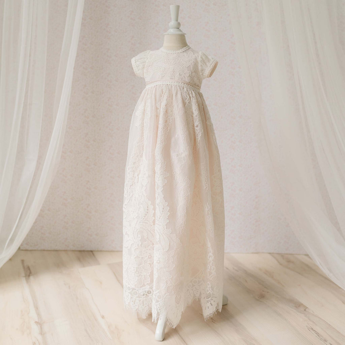 Full length view of the Victoria Christening Gown on a mannequin against a neutral background. Details show the embroidered ivory floral lace with cording and scalloped lace at the hem. Part of the Baptism Gown Girl Collection.
