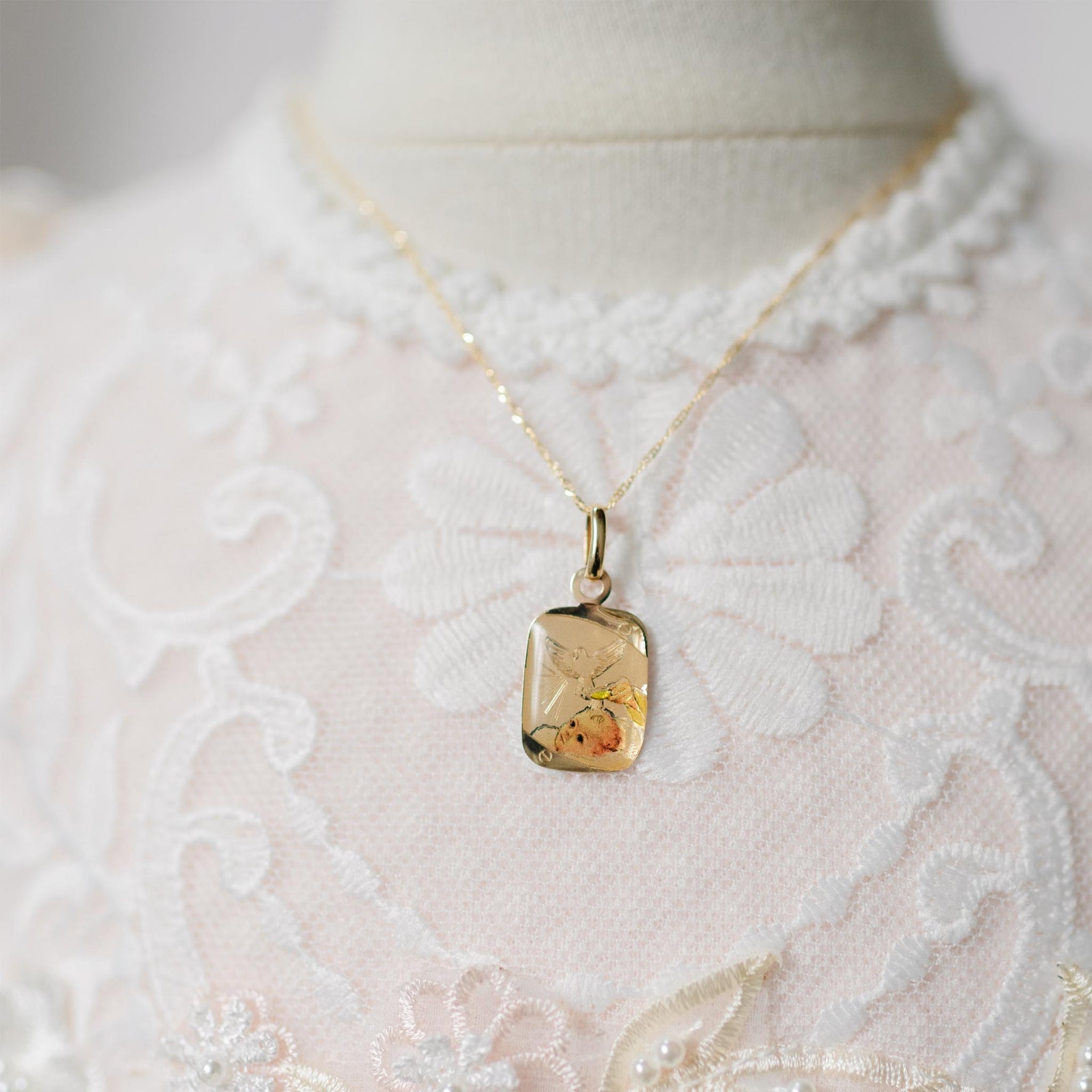 Gold necklace with a pendant on a mannequin wearing a lace garment.