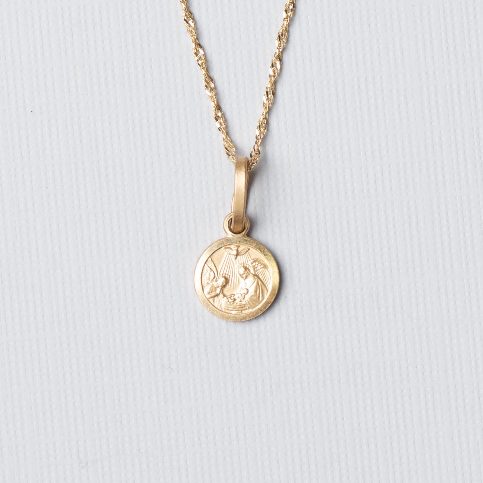 Gold necklace with a round pendant on a light gray background