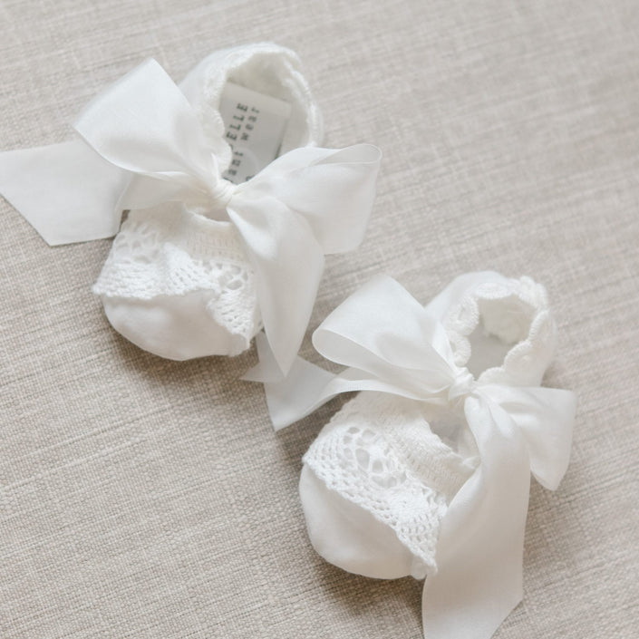 White baby booties with lace details and ribbons on a beige surface