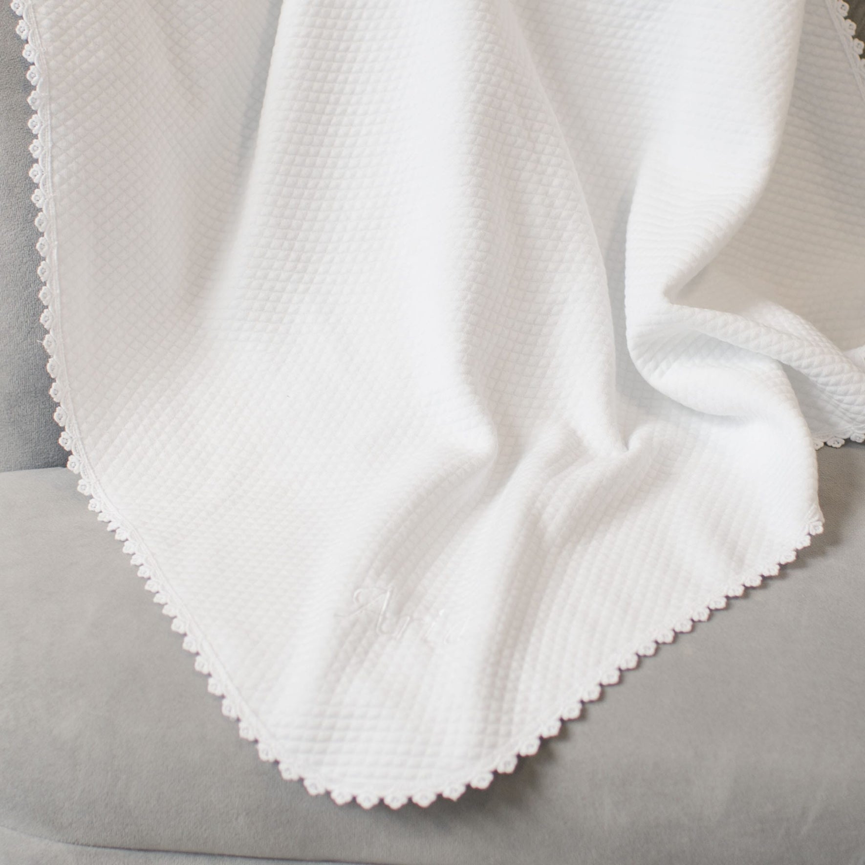 The Aria Personalized Blanket, featuring a textured pattern and scalloped edges, is draped over a grey surface. The fabric appears soft, with edges showcasing delicate stitching, making it an ideal personalized gift.