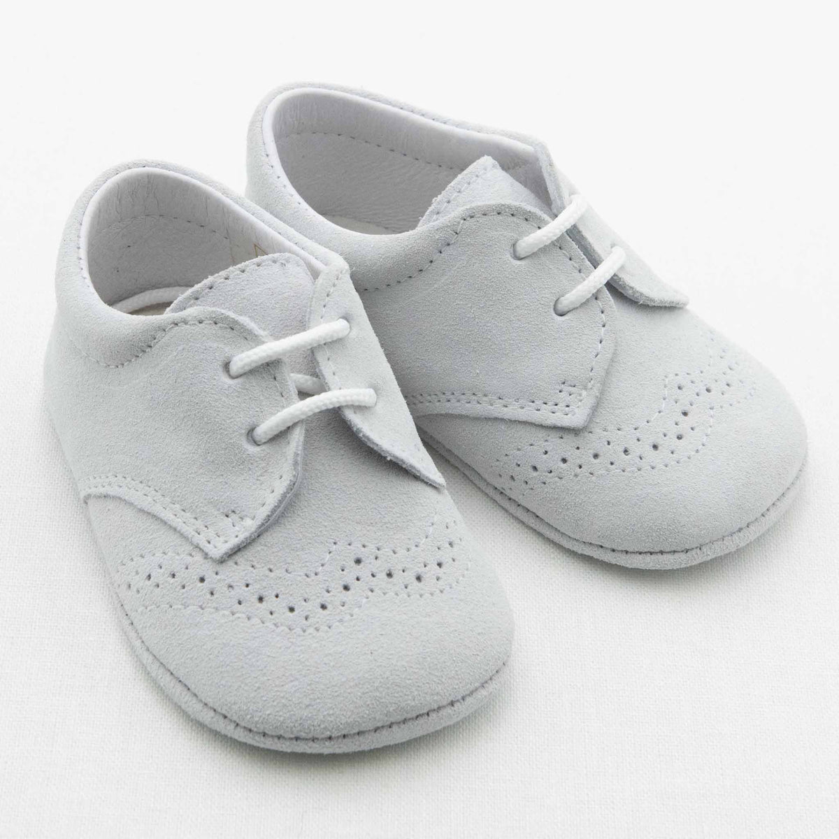 A pair of light gray Asher Suede Shoes from Baby Beau & Belle, designed as mini Oxfords with laces. These handmade baby shoes feature decorative perforations on the toe area and seams, crafted from a soft suede-like material. They are set against a plain white background.