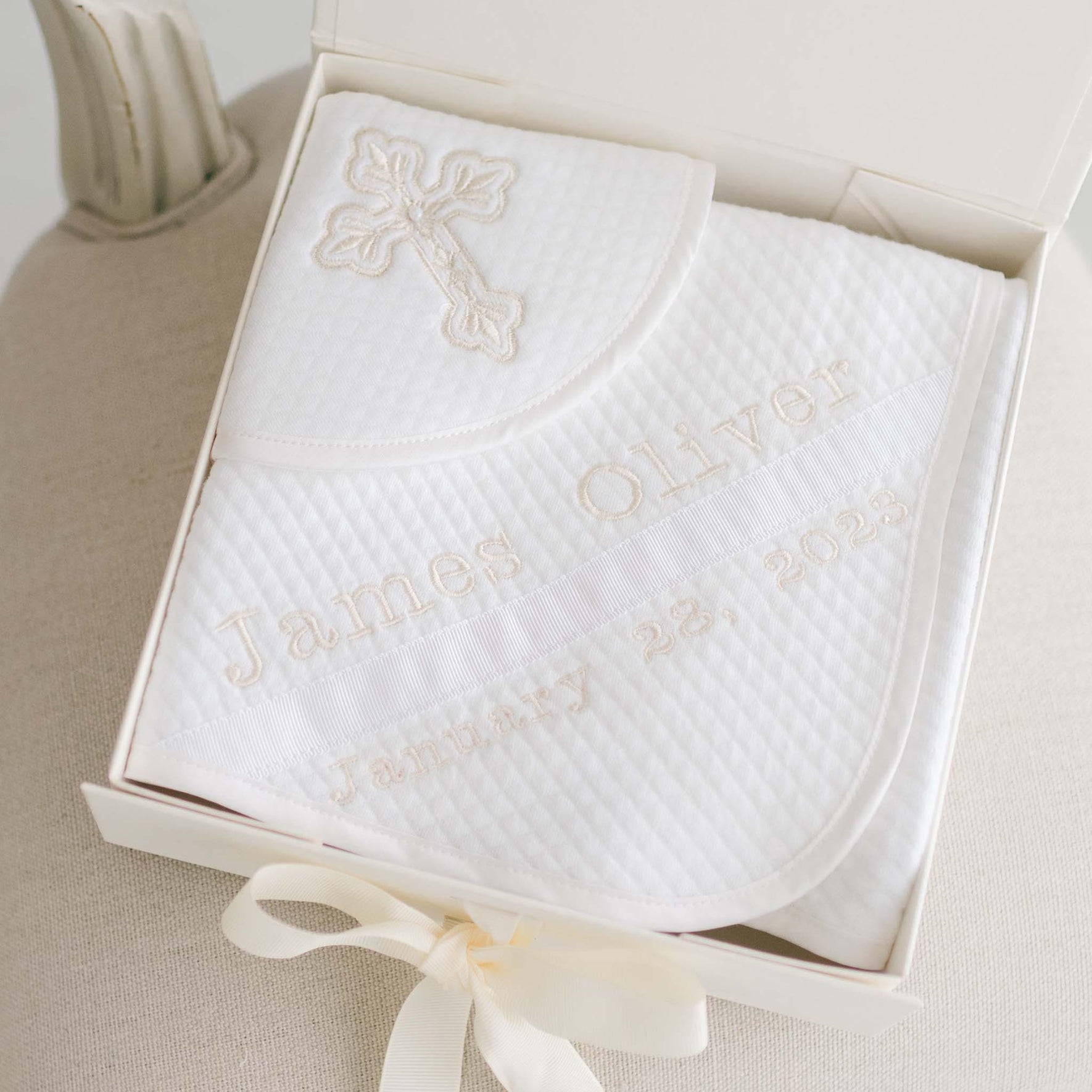 Introducing the Baby Boy Blessing Gift Set: a personalized white quilted cotton blanket elegantly embroidered with a cross and "James Oliver January 28, 2023," presented neatly folded in an open box accented with a ribbon.