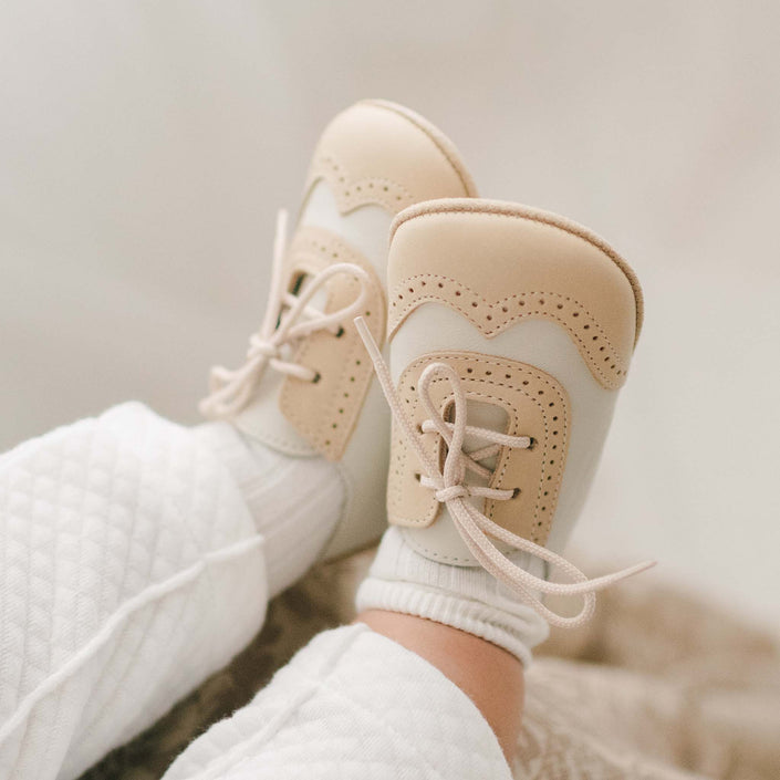 Baby wearing a pair of the Beige and Ivory Wingtip Shoes made with a tan and ivory matte leather with tan suede soles and detailed edging
