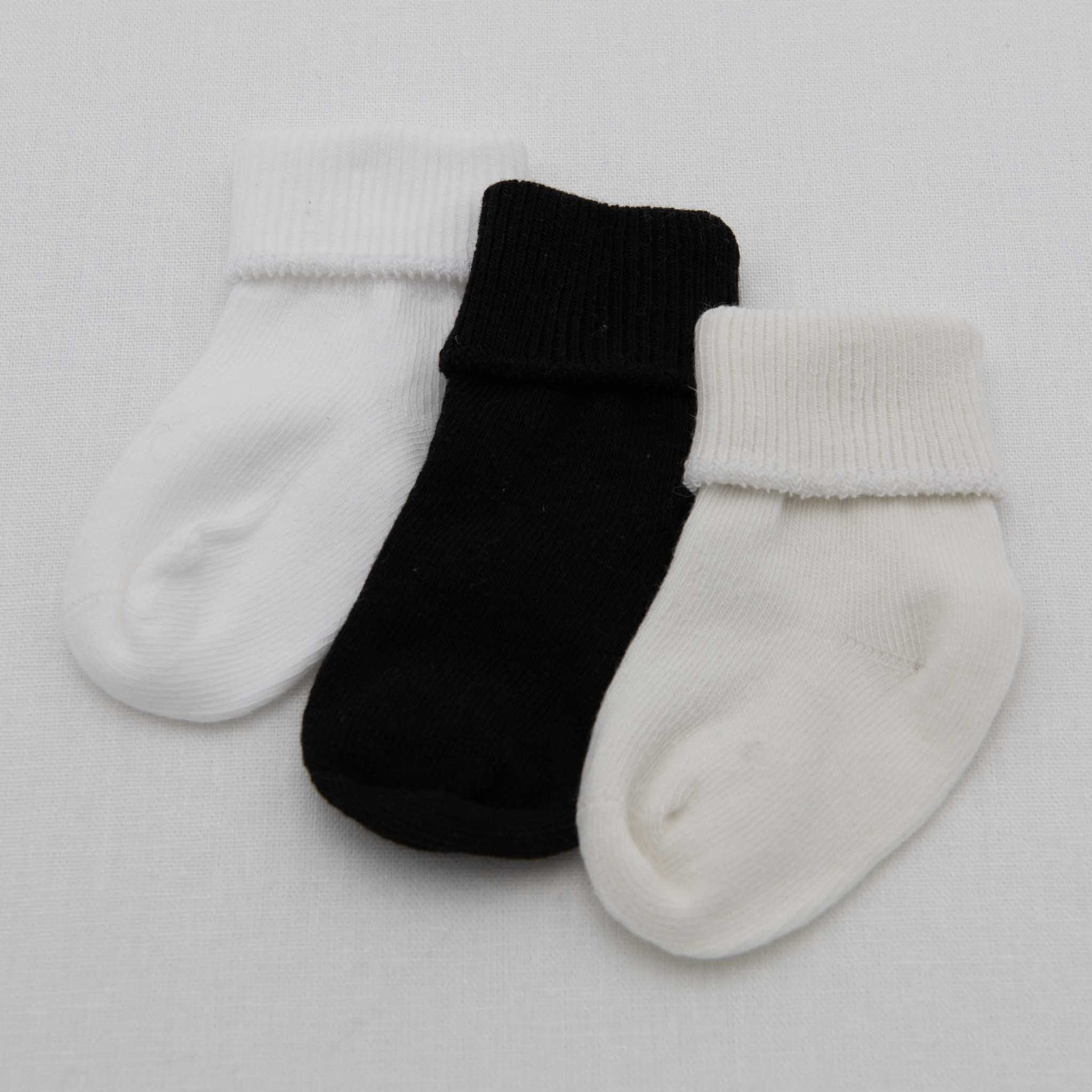 A set of three Boys Simple Socks made of soft cotton is arranged on a white surface: a white sock on the left, a black sock in the center, and another white sock on the right. Their cuffed tops add charm to any little one's outfit.