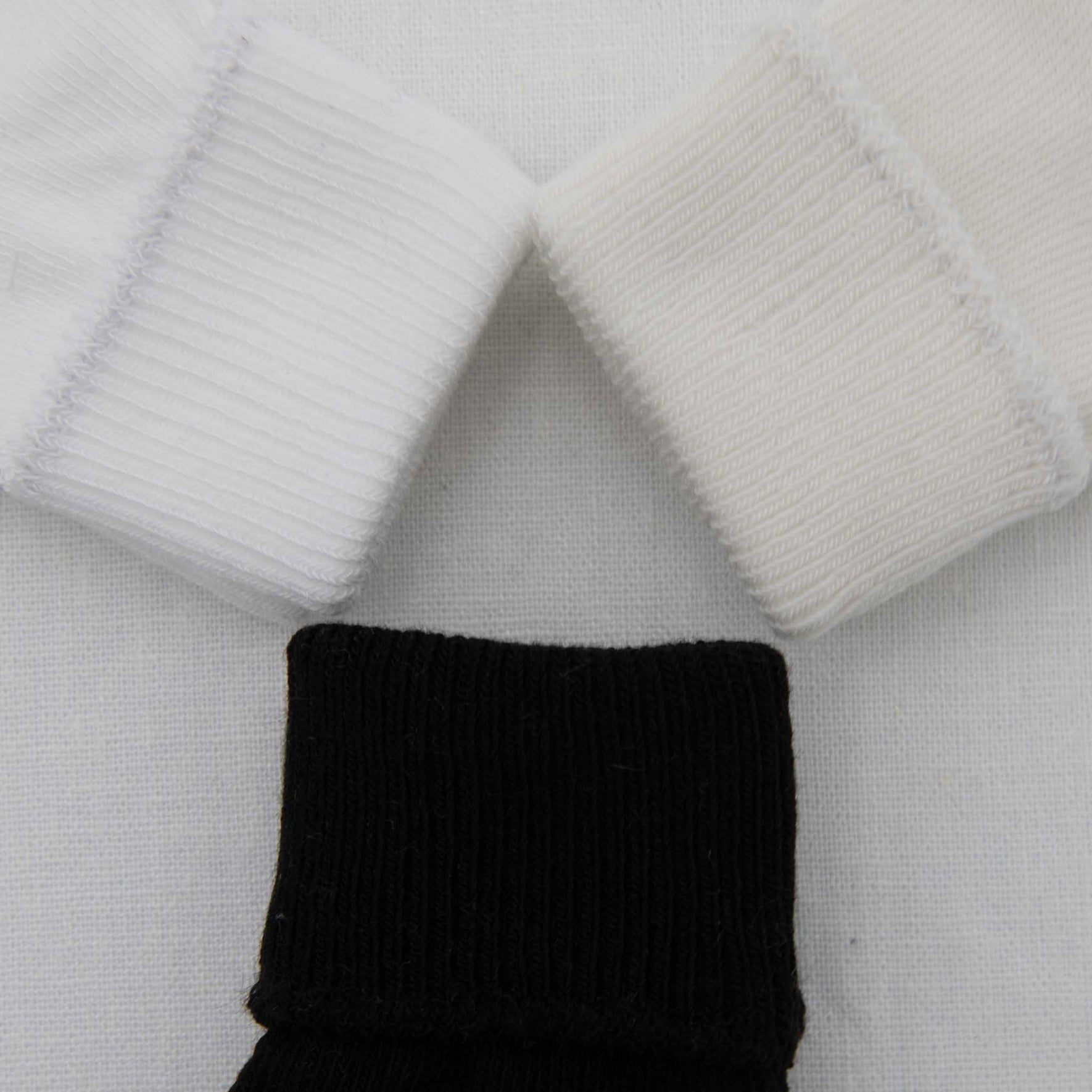 Three Boys Simple Socks are displayed in a triangular formation on a white surface. The two top socks are cotton white, while the bottom sock features a ribbed black design. Their cuffs are prominently visible, enhancing the texture of this soft ensemble.