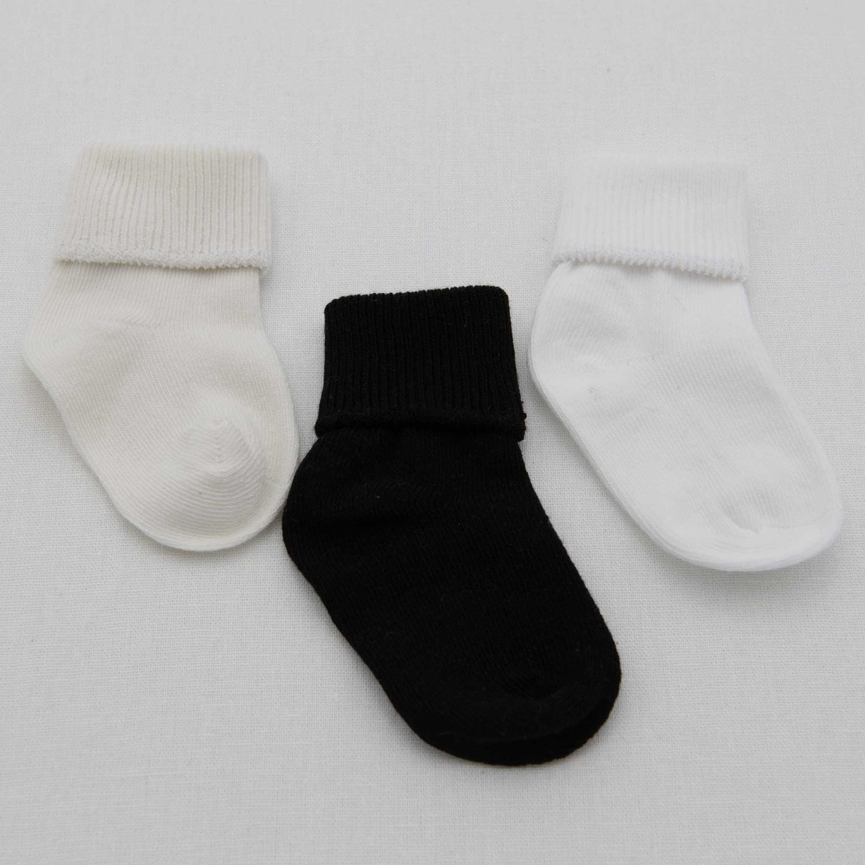 Displayed on a white background are three Boys Simple Socks, crafted from gentle cotton. Arranged horizontally, the set features two white socks on the left and right and a contrasting black sock in the center, forming an adorable little ensemble.