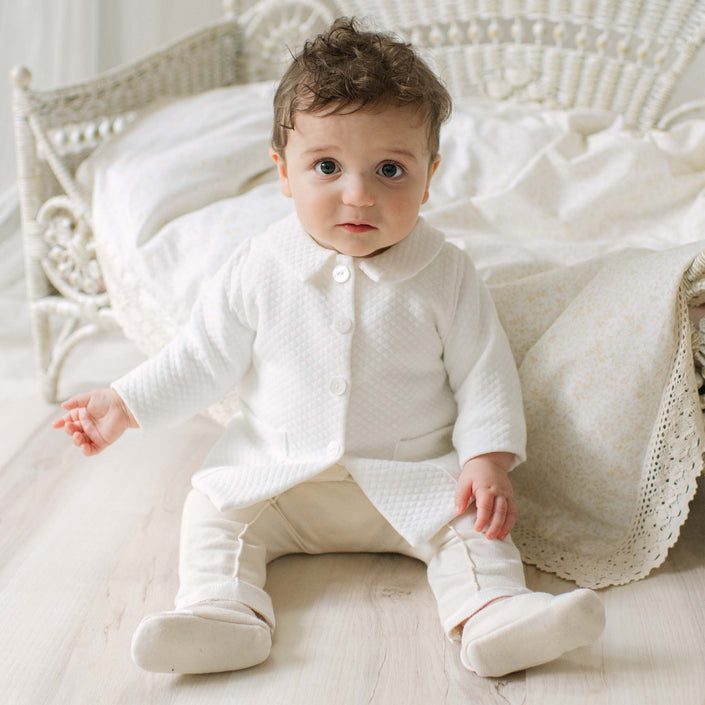 Baby in the Braden Coat Suit sitting on a wooden floor with a white wicker chair and patterned blanket in the background. Perfect choice for high end baby boy suits. 