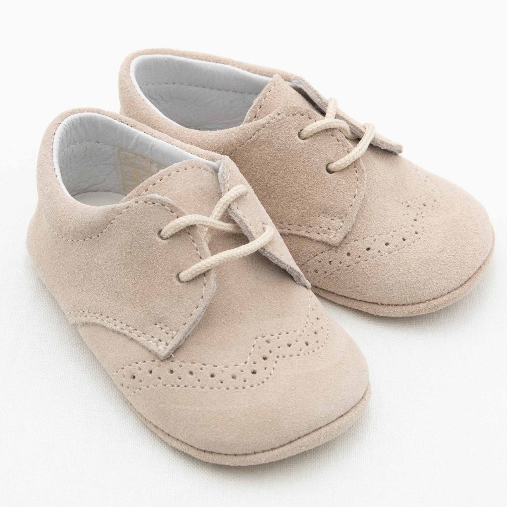 A pair of Camel Suede Shoes from Baby Beau & Belle, designed for boys with laces and intricate decorative stitching details. These shoes, with their handcrafted appearance, are made from a soft suede-like material and are set against a plain white background.