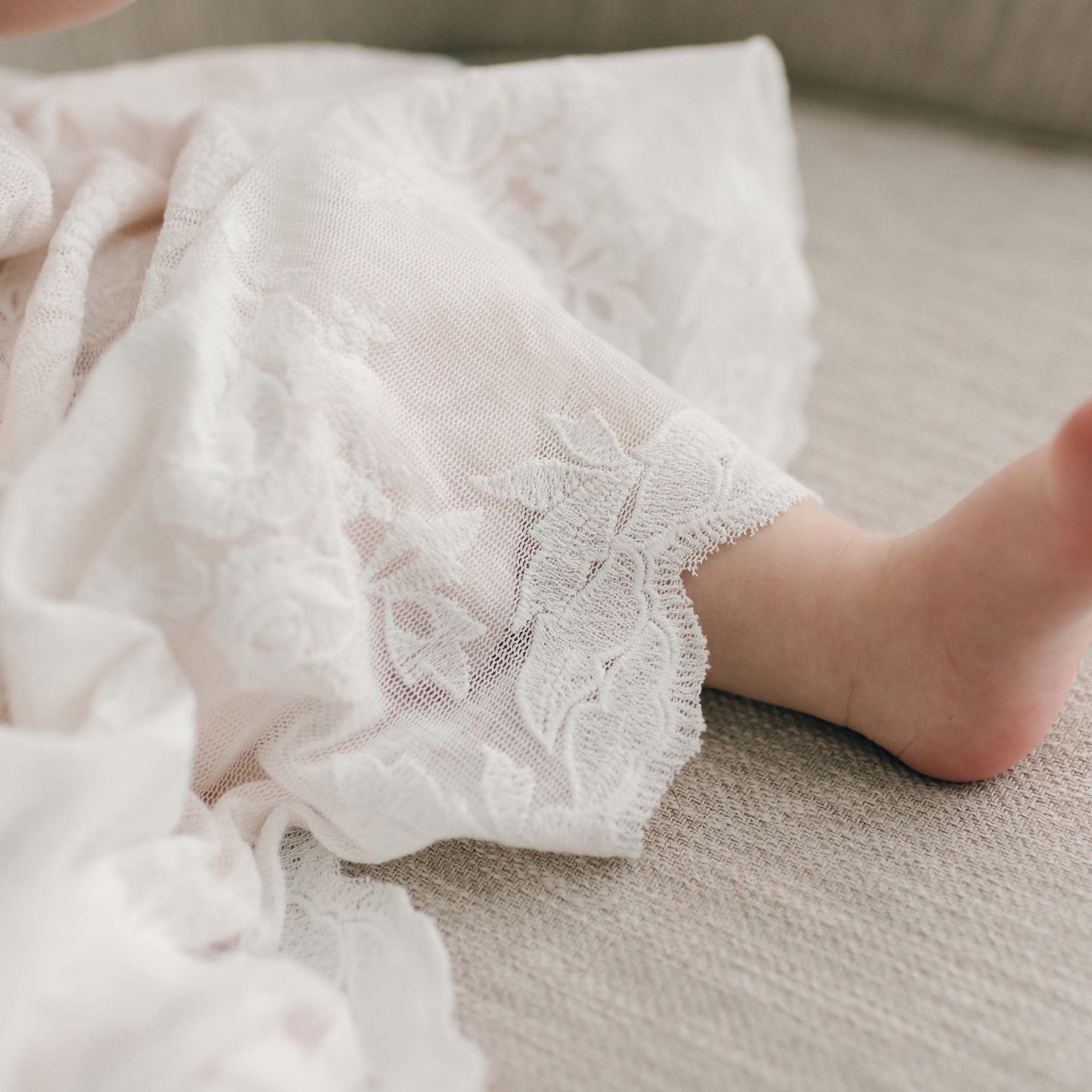 Christening Gown with cotton lace scallop hem on baby girl sitting on beige chair