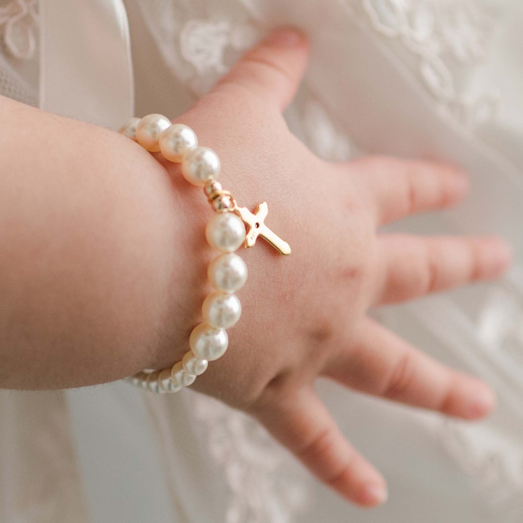 Close detail of Cream Luster Pearl Bracelet with Gold Cross on a baby girl's wrist.