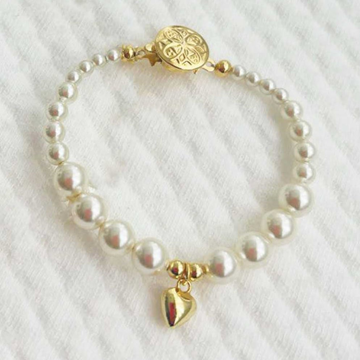 Cream pearl baby bracelet with gold plated heart charm on a white textured background