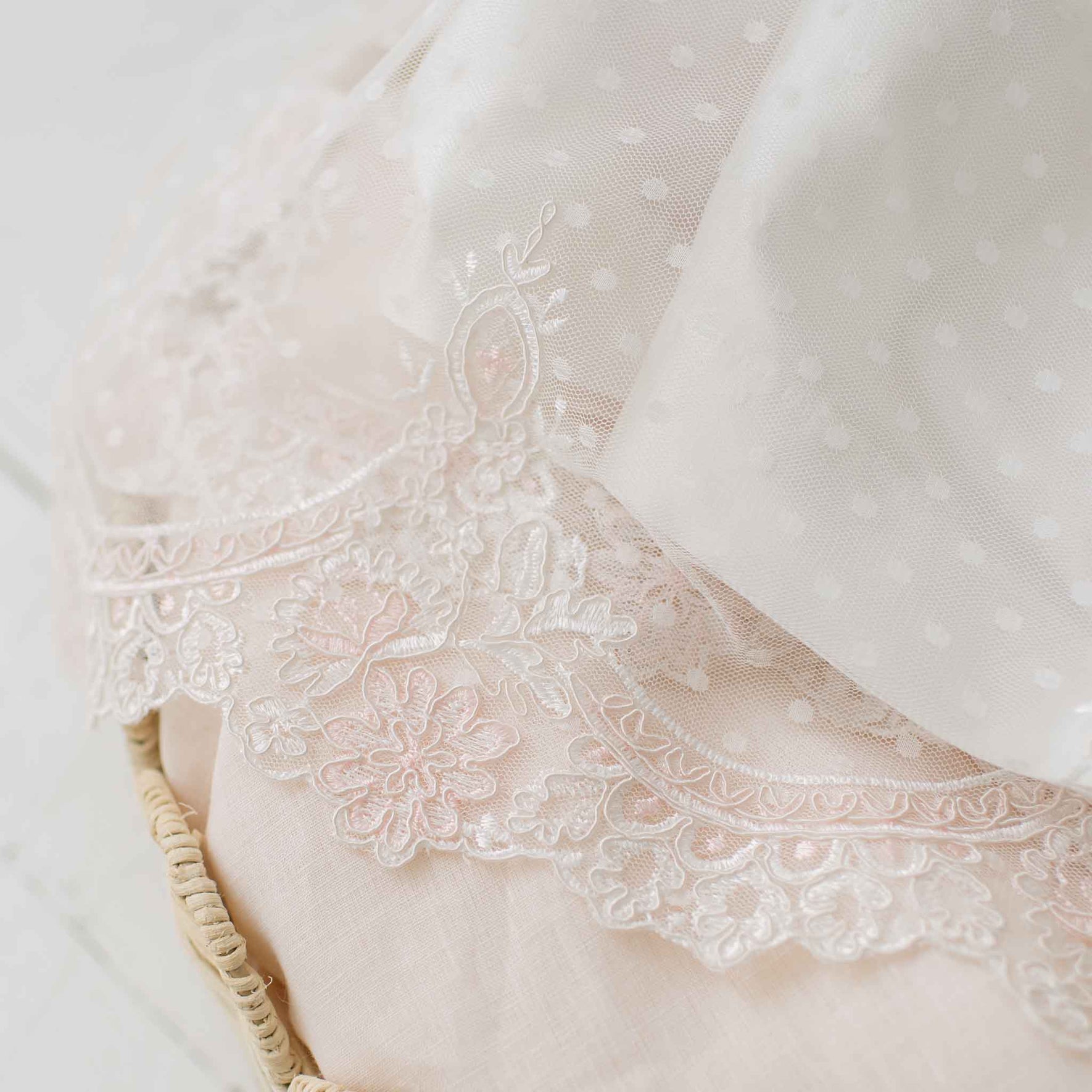 Close-up of the scalloped lace at the hem of the skirt on the Elizabeth Newborn Christening Gown showcased atop a pink linen lined crib.