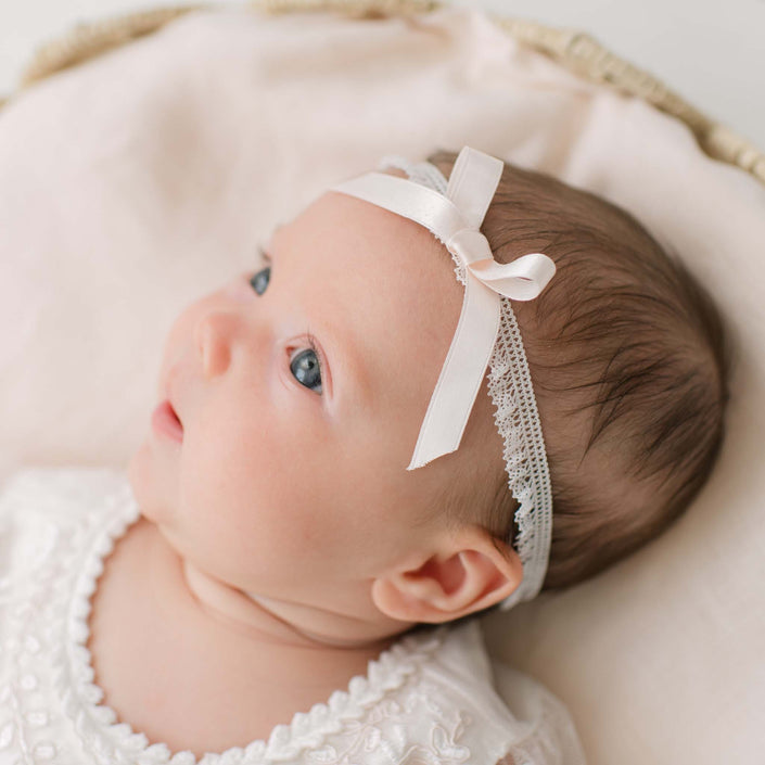 Newborn baby wearing an Elizabeth Silk Ribbon Headband with a pink silk ribbon bow, lying on a soft surface.