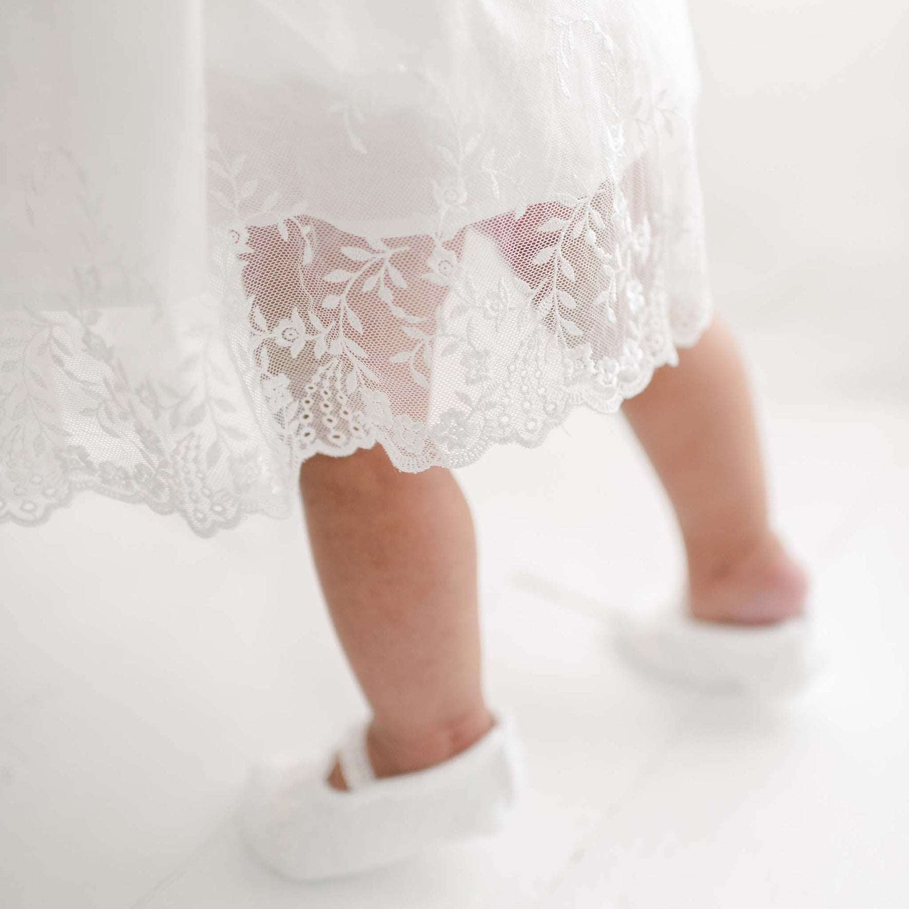 A close-up image of a baby wearing an Ella Romper Dress standing, showing only the legs and feet.