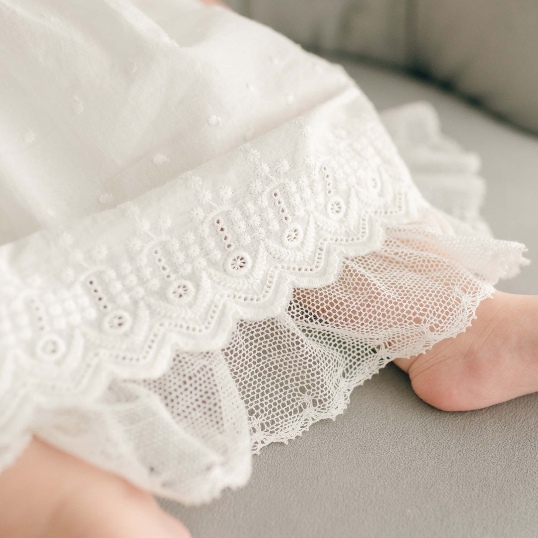 A close-up of the dress hem, revealing intricate lacework and scalloped embroidery over delicate mesh fabric.