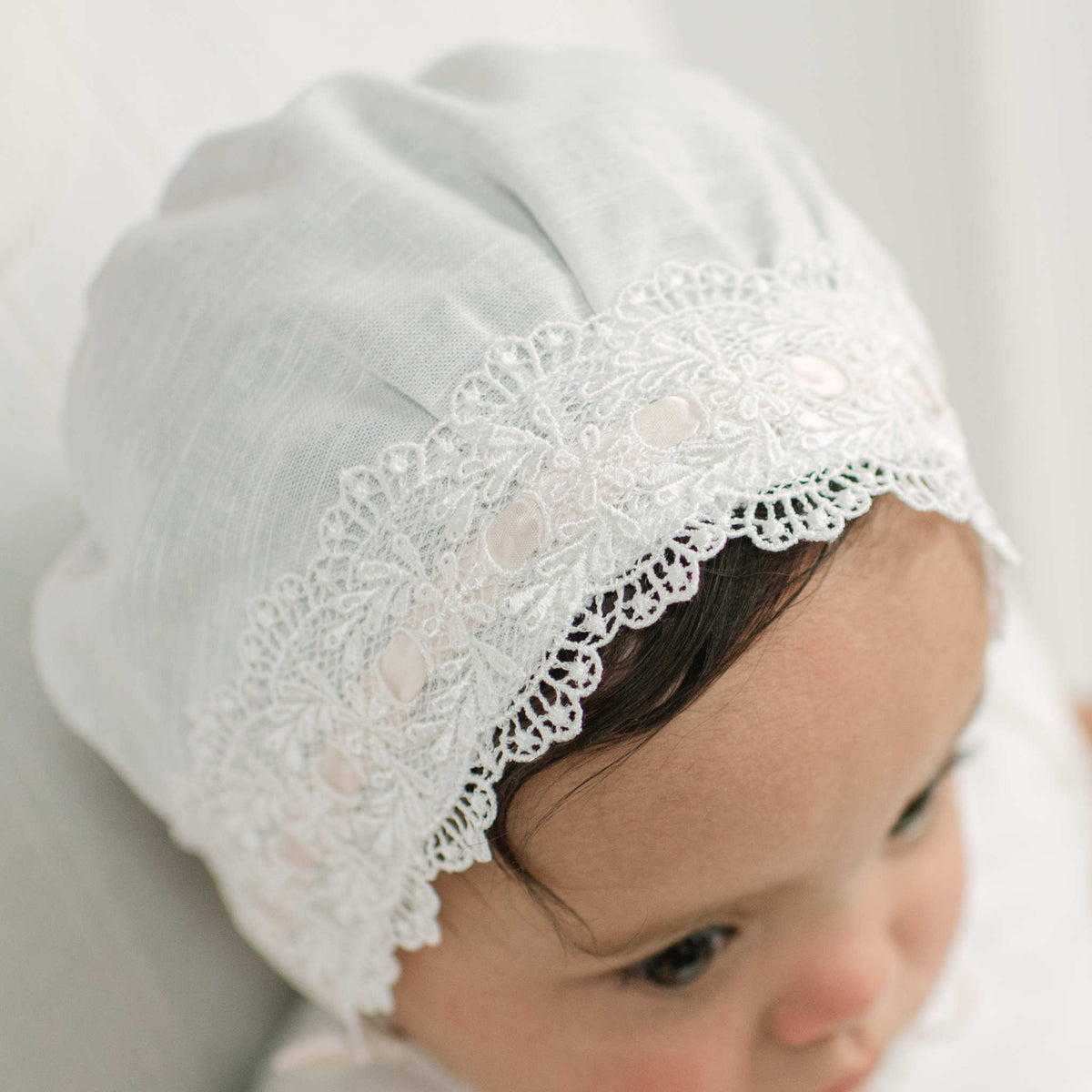 A close-up of a baby wearing a ivory linen bonnet with delicate lace trim 
