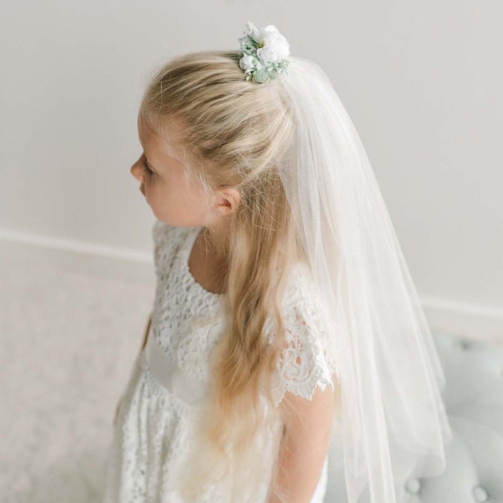 A girl wears the First Communion Veil, secured with a white floral headpiece.