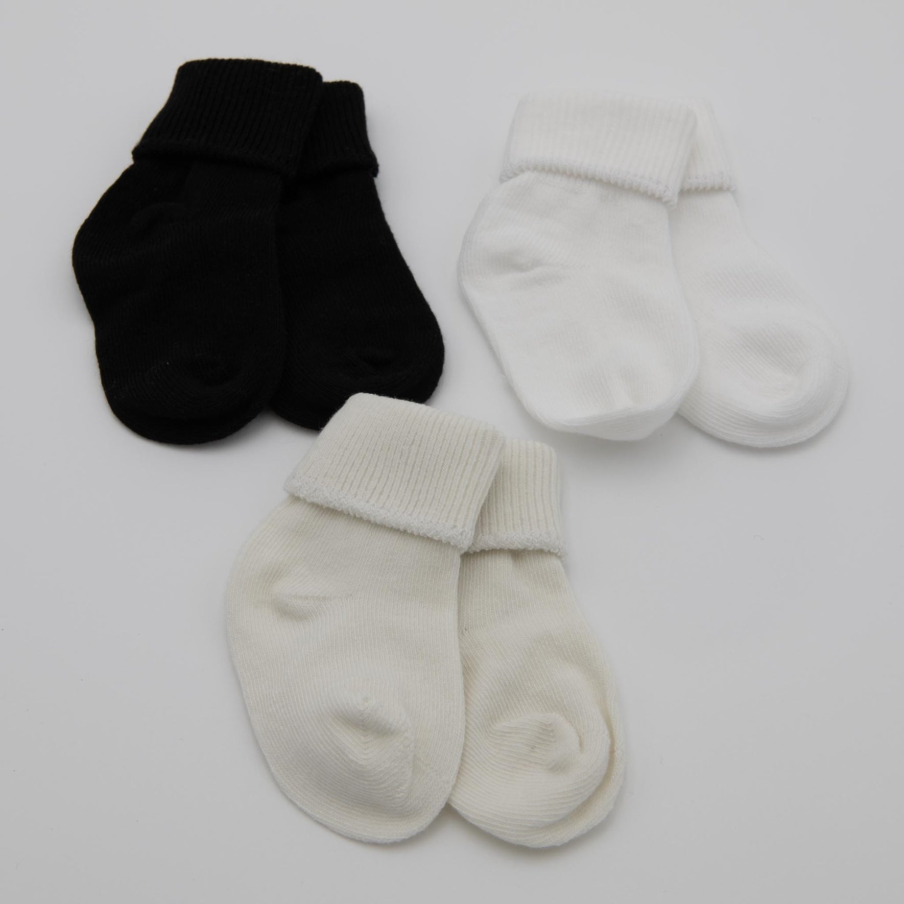 The Girls Simple Socks, composed of a cotton nylon spandex blend for an ideal baby outfit, are displayed against a white background. The set includes three pairs: one black pair and two white pairs, each with neatly folded cuffs.