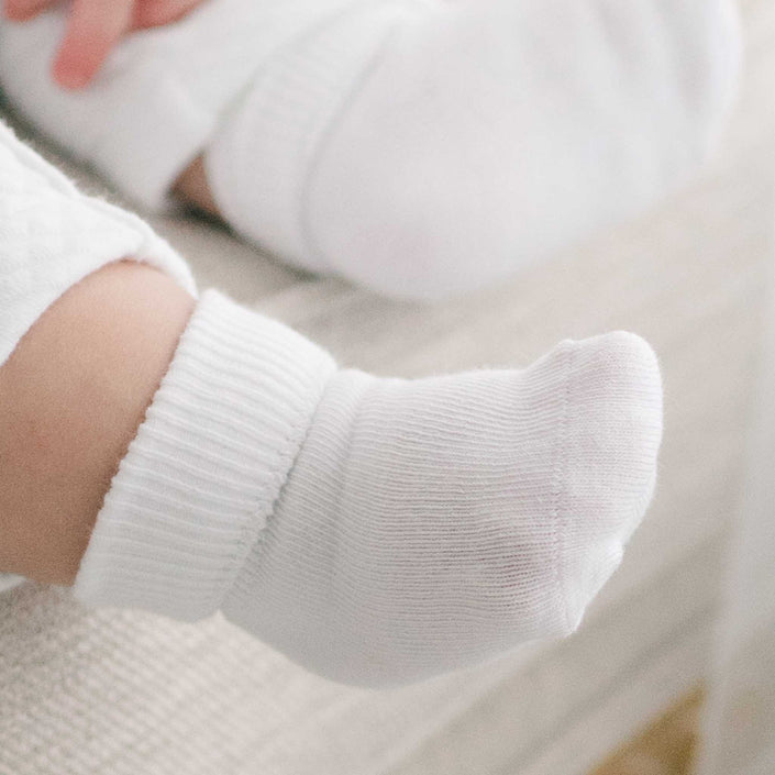 Close-up of a baby's foot wearing Girls Simple Socks, crafted from cotton nylon spandex, resting on a light-colored surface. The foot and sock are sharply in focus against a softly blurred background.
