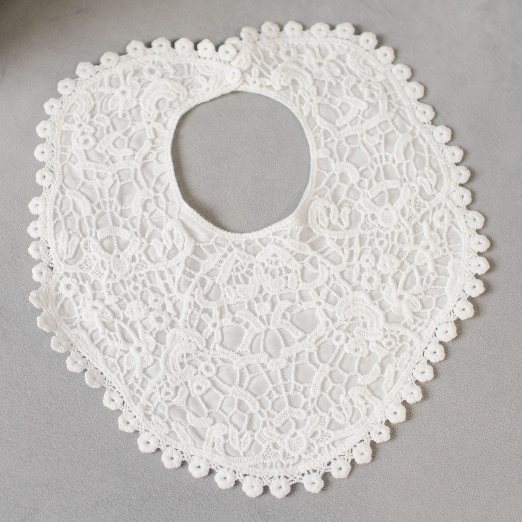 A white lace baby bib featuring intricate floral patterns and scalloped edges is elegantly displayed on a gray surface, perfectly complementing the Grace Accessory Bundle - Save 15%.