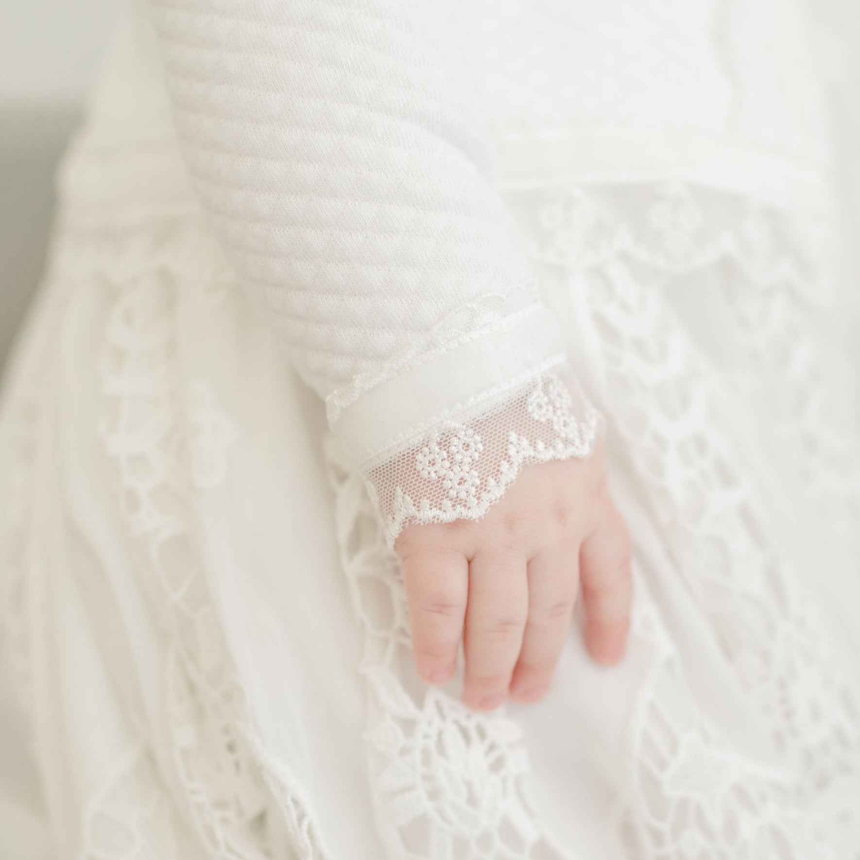 A close-up of a child's hand resting on the Grace Quilted Cotton Sweater, showcasing its intricate quilted design and soft, delicate fabric around the wrist. The focus is on the refined craftsmanship and elegance of this beautiful sweater.