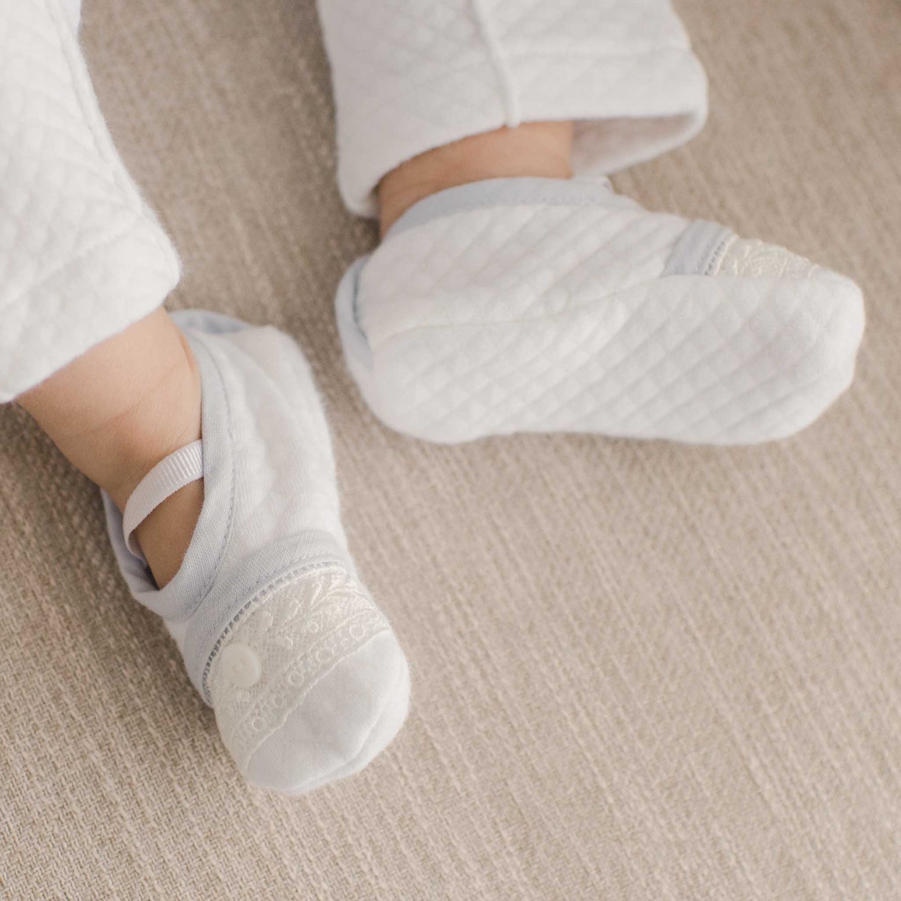 Harrison Christening Booties on a baby's feet, complemented by soft quilted fabric and intricate lace detail.