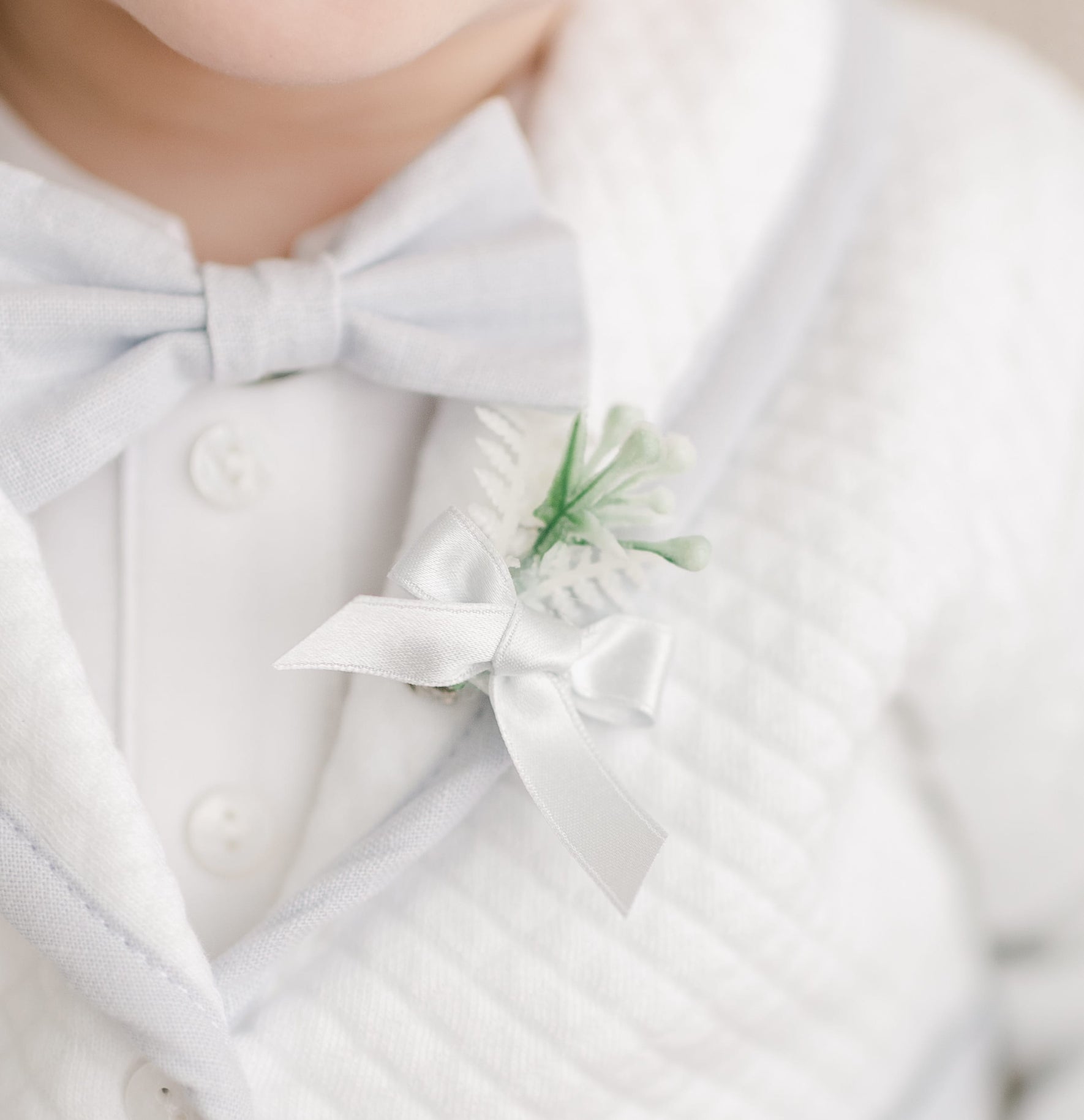 Close-up of the Harrison Christening Bow Tie & Boutonniere, featuring a light blue bow tie and a boutonniere with white ribbon and green accents, styled as part of a christening outfit.