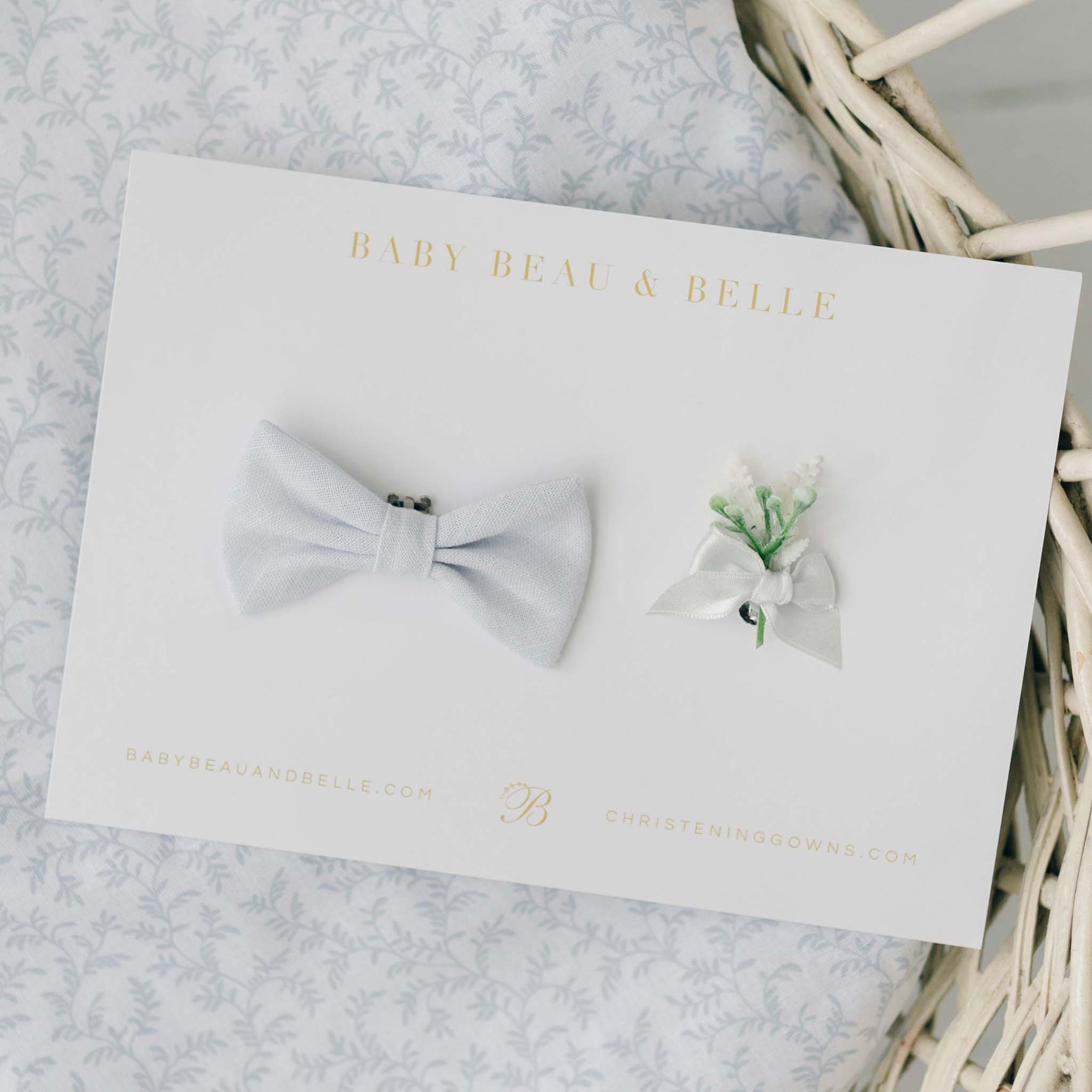 The Harrison Christening Bow Tie & Boutonniere set, showcasing a pale blue linen bow tie and a boutonniere with white ribbon and green sprigs, elegantly presented on a branded Baby Beau & Belle card.
