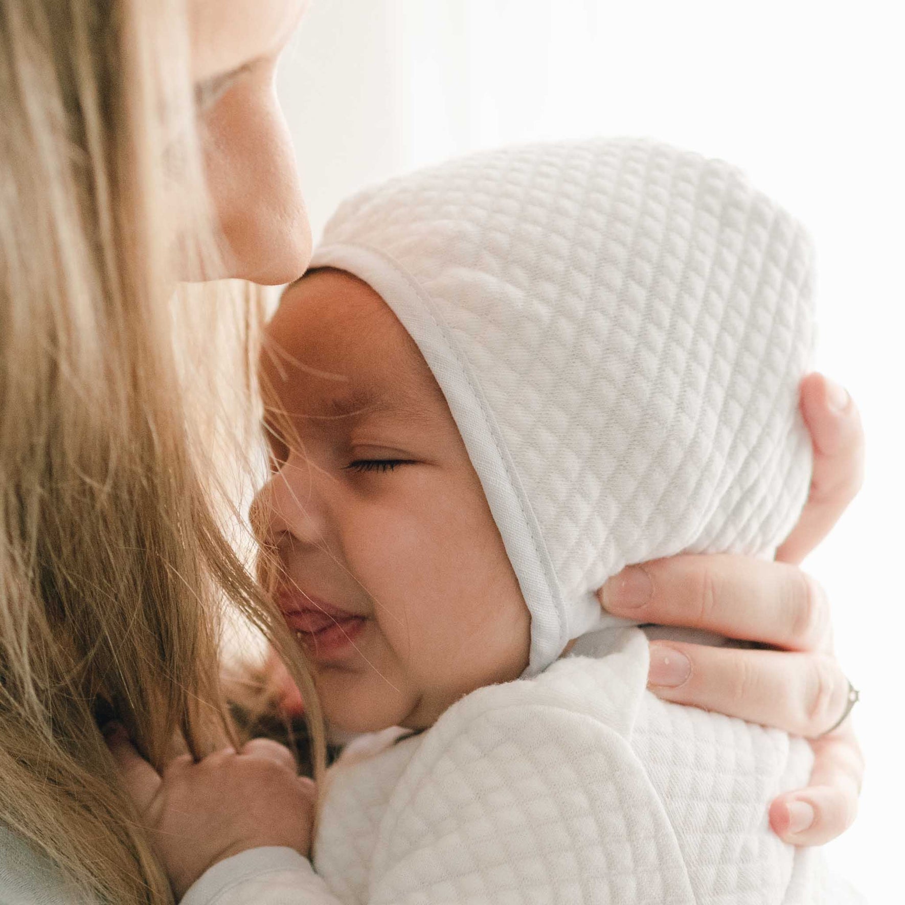 Baby nestled close, wearing the Harrison Quilted Bonnet, emphasizing its comfortable and stylish design.