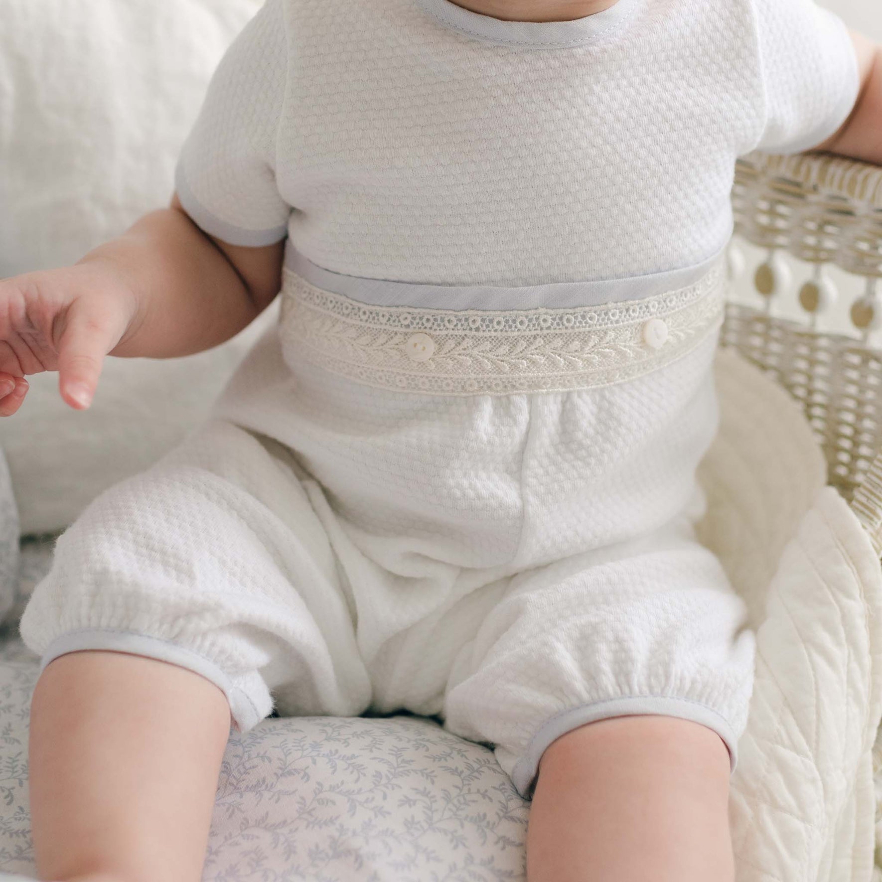 Detailed view of the Harrison Short Sleeve Christening Romper highlighting the quilted fabric texture, intricate lace trim on the waistband, and subtle light blue edging.