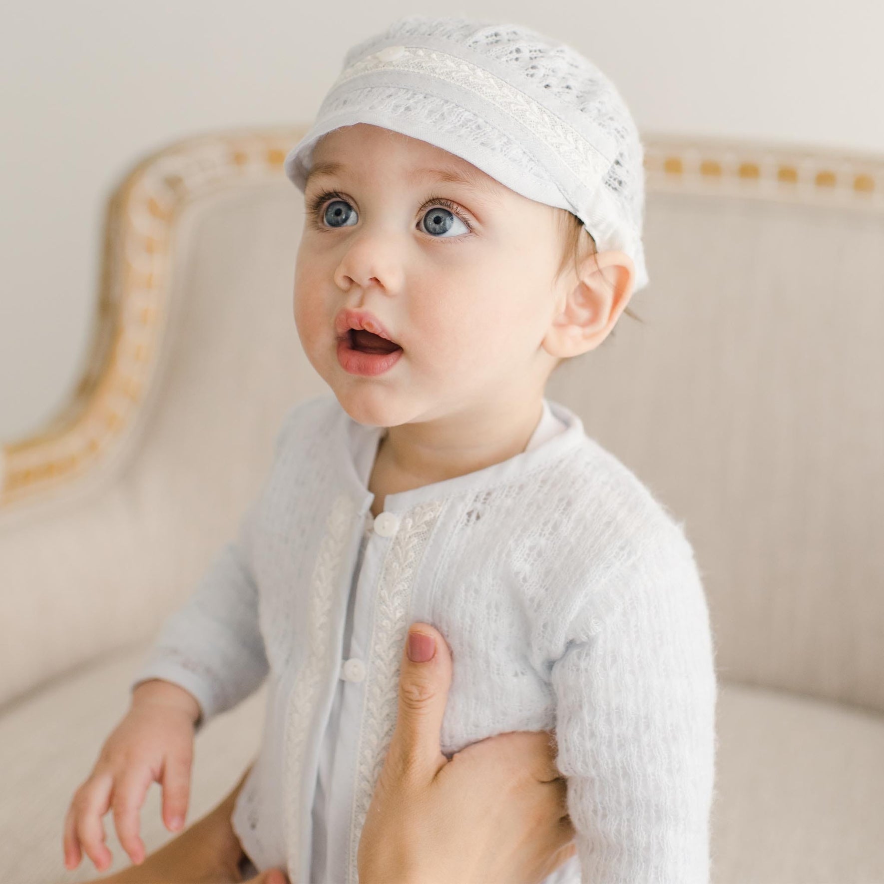 Close up view of a baby wearing the Harrison Sweater 3-Piece Pants Suit, emphasizing the soft lace accents on the sweater and matching cap.