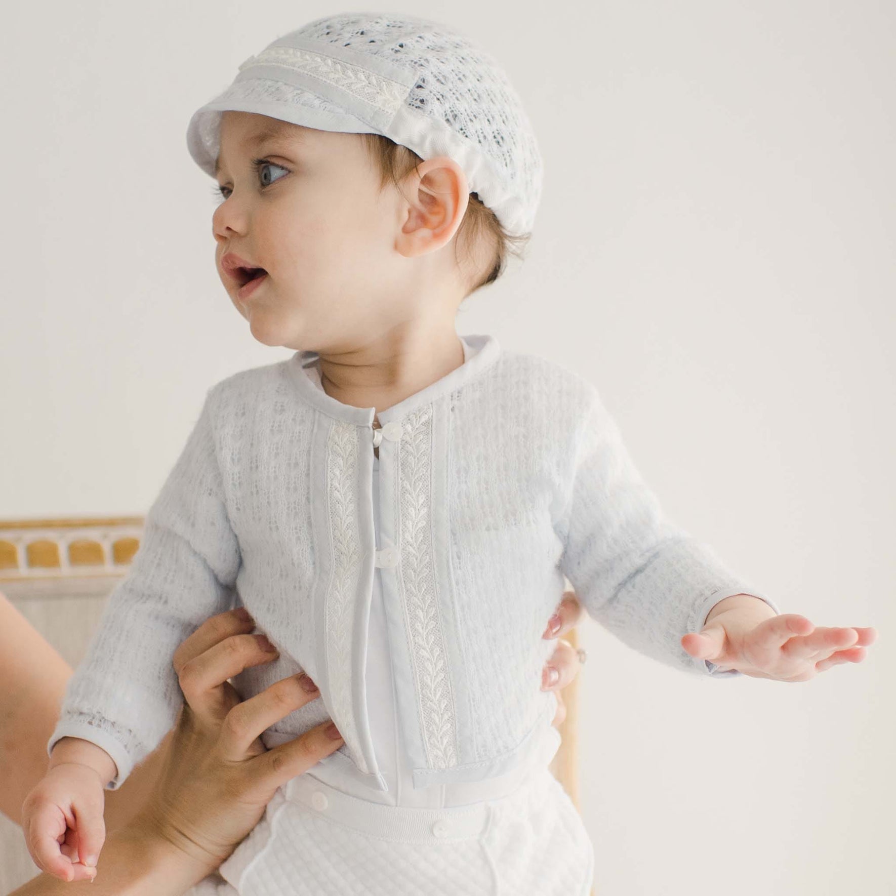 Side profile of a baby wearing the Harrison Sweater 3-Piece Pants Suit, emphasizing the soft lace accents on the sweater and matching cap.