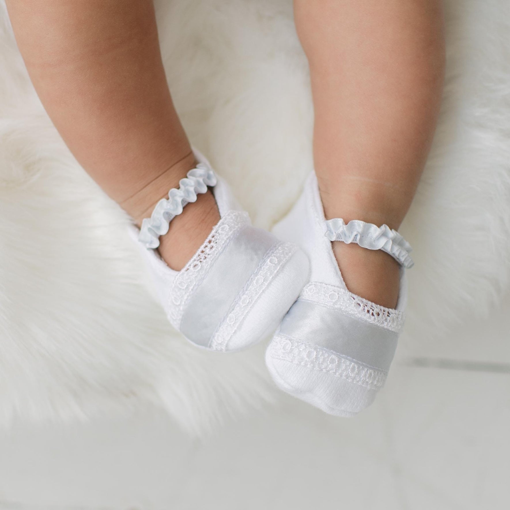 Close up photo of a baby wearing the Henry booties against a soft white background. Details show custom blue ribbon and Venice lace detailing across the toes. Perfect baptism gift from godparents.