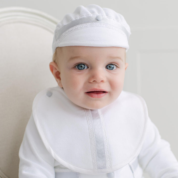 Baby wearing a white bib with blue lace detail over a white outfit.
