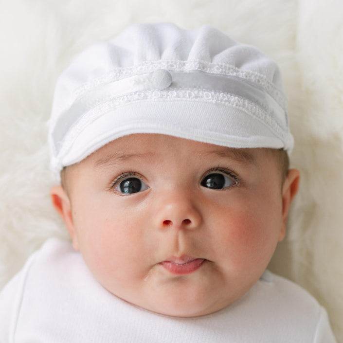 Baby wearing the Henry Brim Cap with lace details on a plain background.