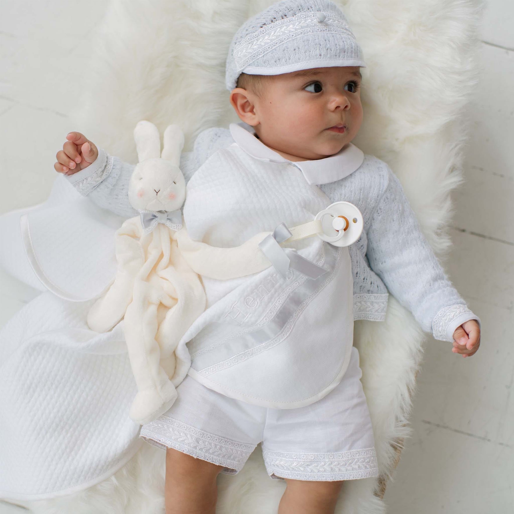 Baby in a light blue outfit with a white plush bunny on a white fur rug.
