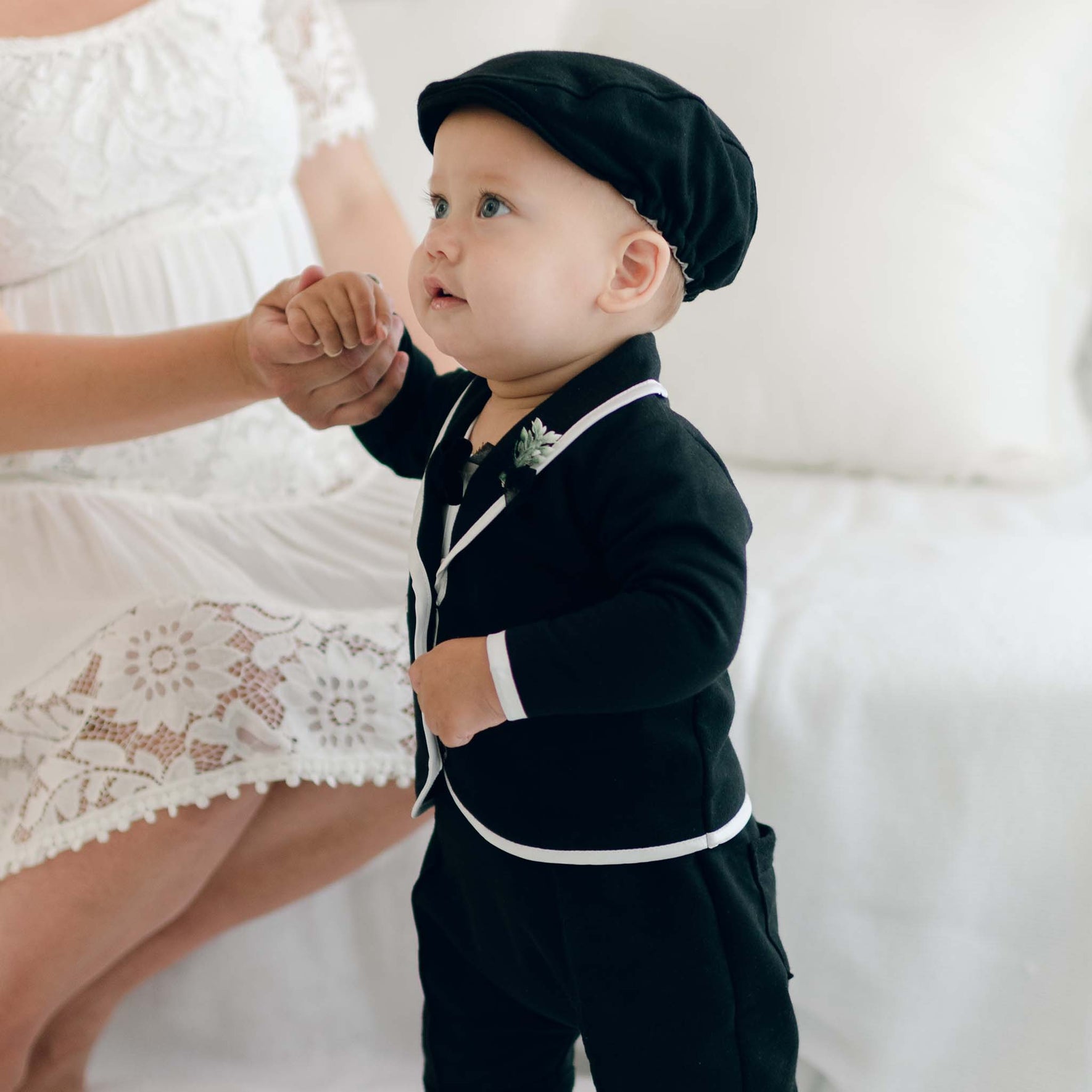 A baby wearing the black James 3-Piece Suit, looking up while holding an adult's hand.