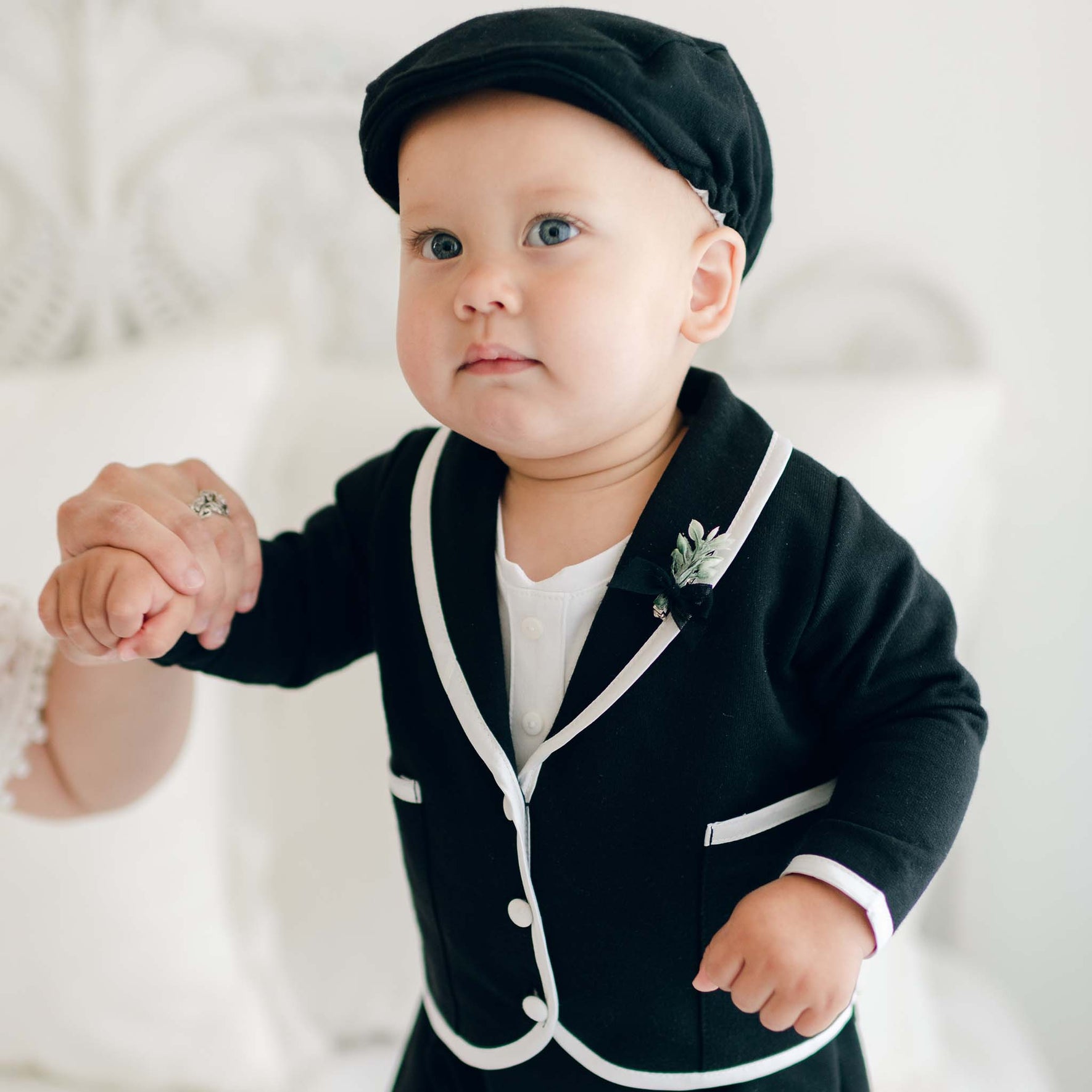 A baby in the black version of the James 3-Piece Suit, standing with a matching black cap and white trim details.