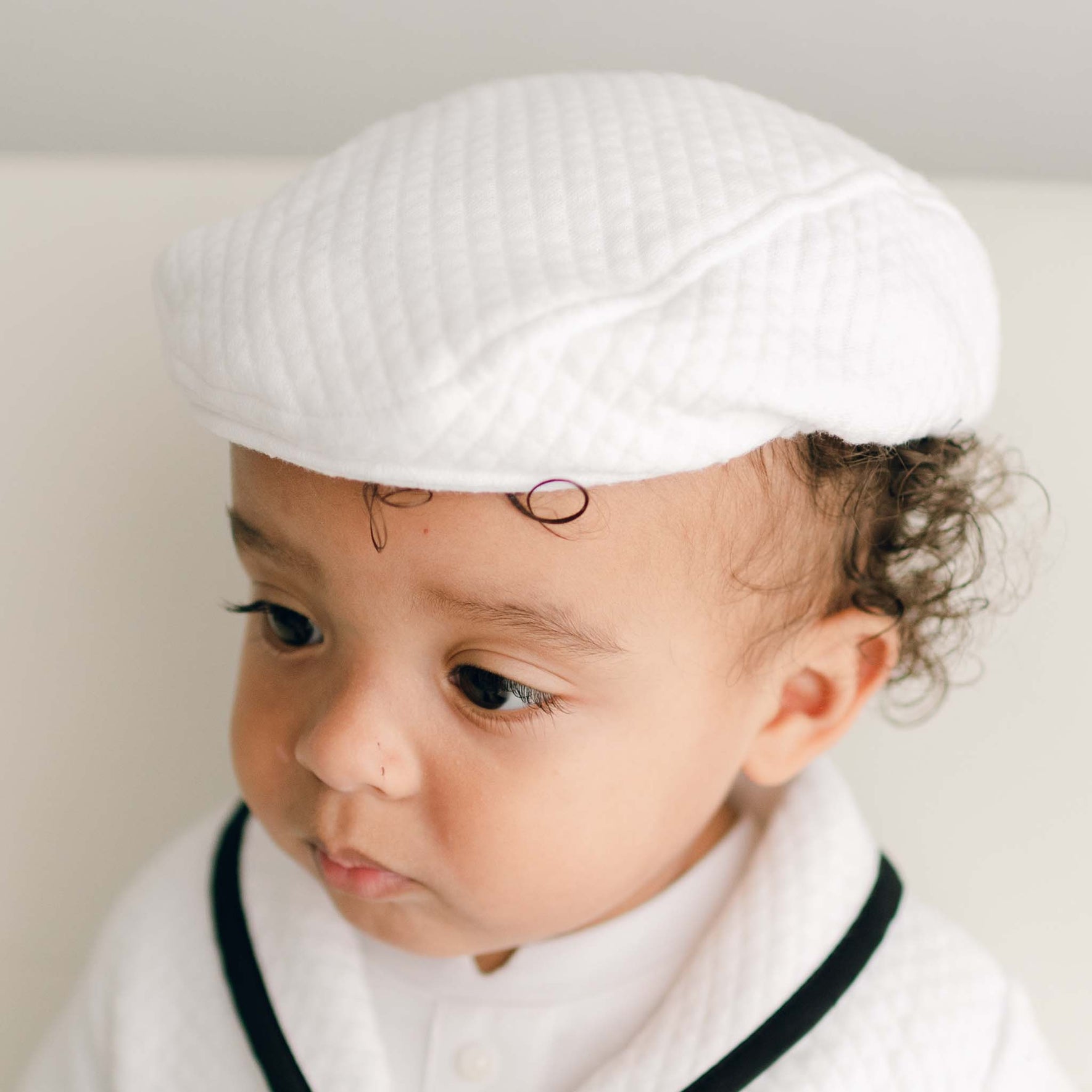 Baby boy wearing the white James Newsboy Cap made from 100% White Quilted Cotton with a soft elastic back.