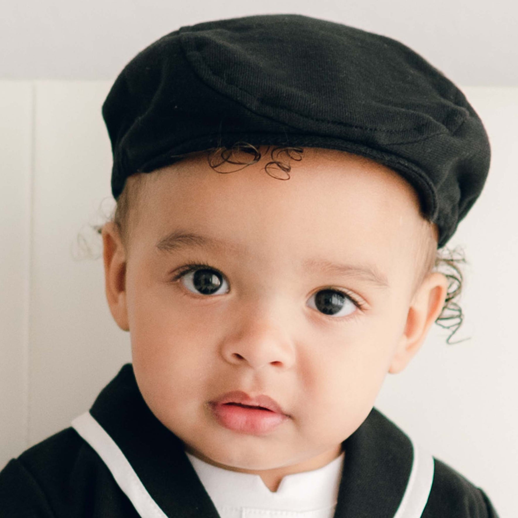 Baby boy wearing the black James Newsboy Cap made from 100% Black French Terry Cotton with a soft elastic back.