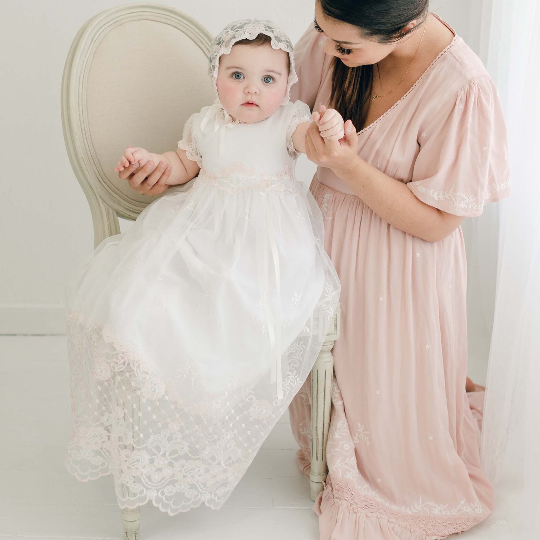 Woman in a pink dress holding a baby in a white and pink lace dress and bonnet.